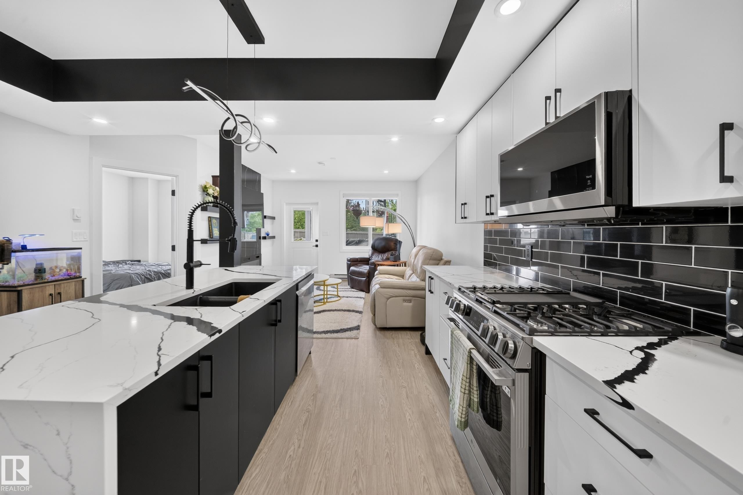 Modern kitchen featuring an expansive island with a large sink, white countertops with prominent veining, matte black cabinetry, stainless steel appliances, and a black subway tile backsplash - 626 Astoria Way, Devon, AB