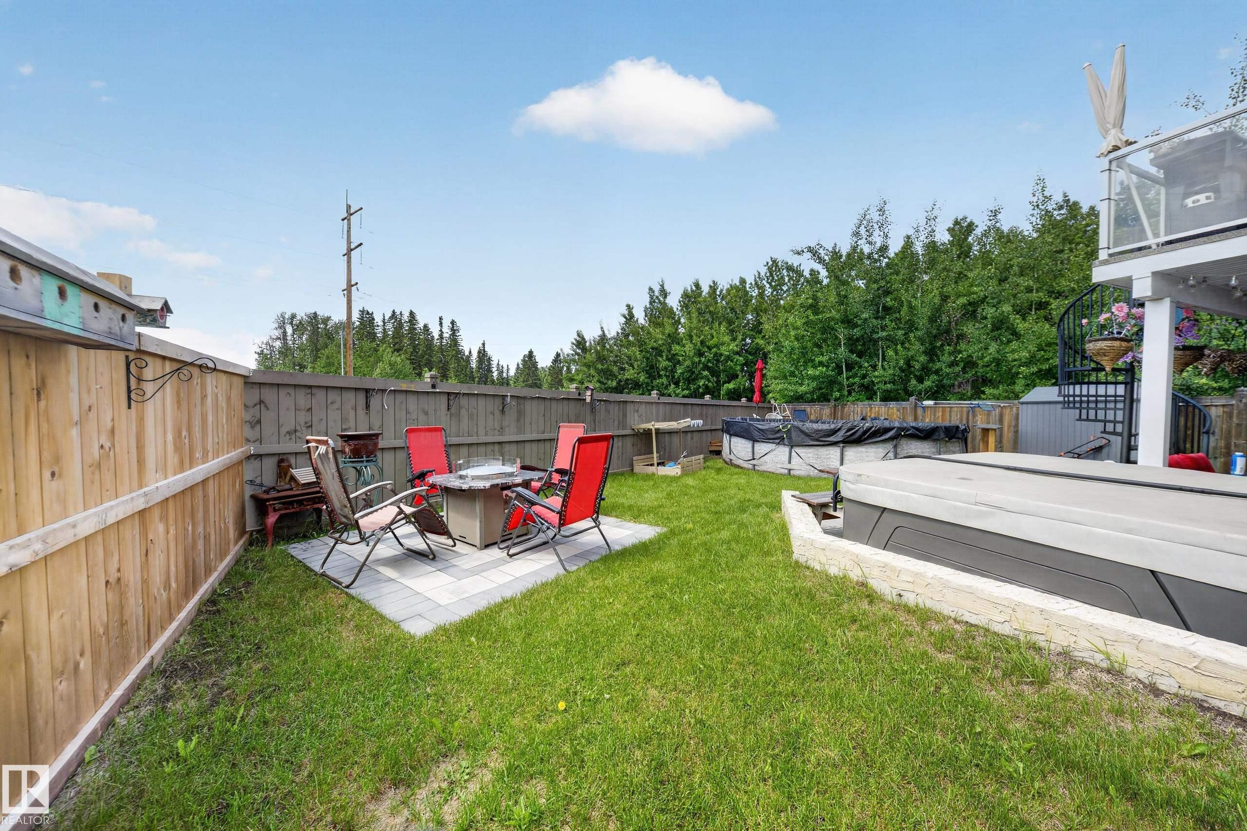 Expansive backyard featuring a stone paver patio, a freestanding fire pit, a mature tree line, a privacy fence, and an above-ground pool - 626 Astoria Way, Devon, AB