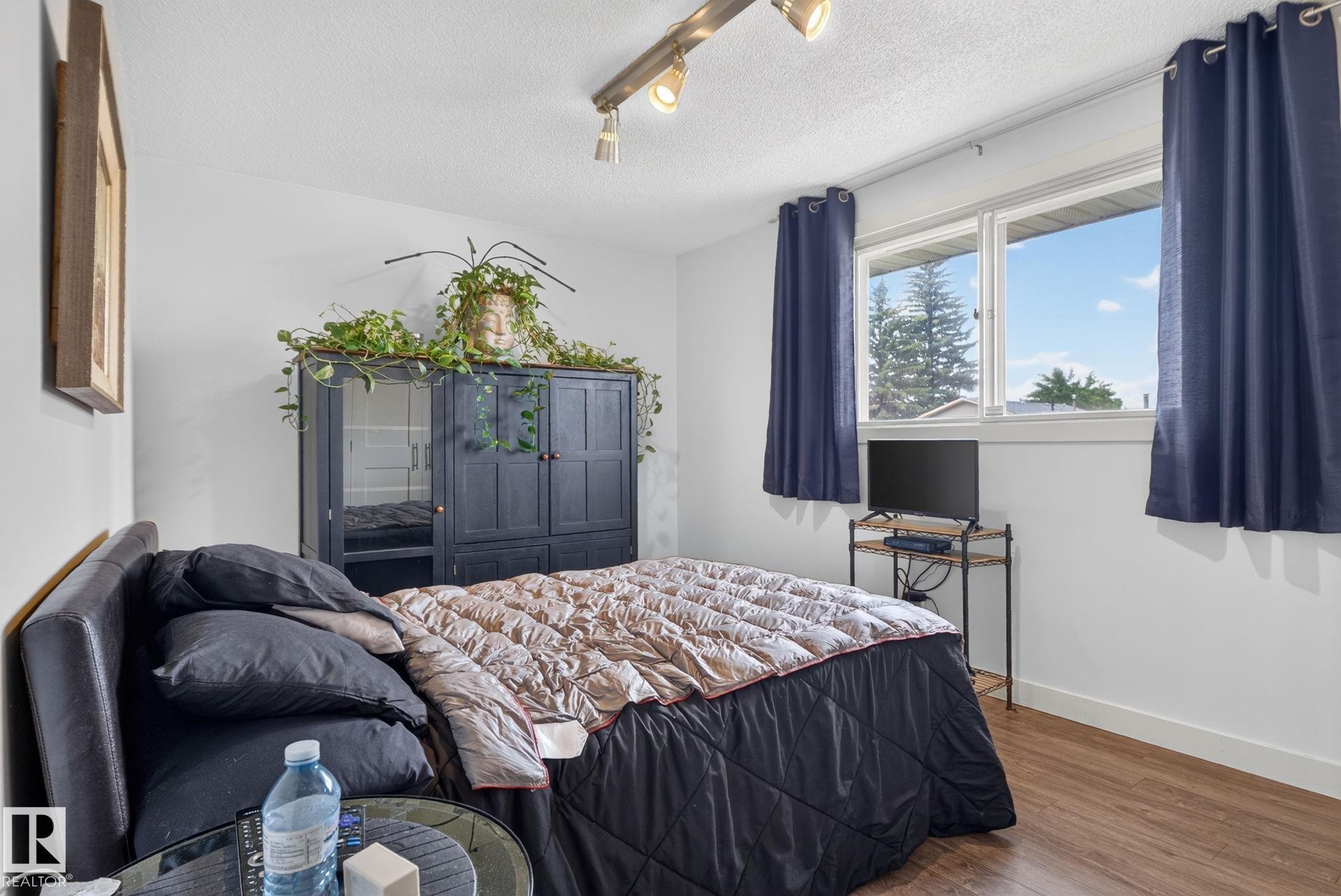 Bedroom featuring wood-finish flooring, a double window, track lighting, and a built-in dark wood wardrobe with mirrored panels - 7539 149A Avenue Nw, Edmonton, AB - Indoor Photo Showing Bedroom