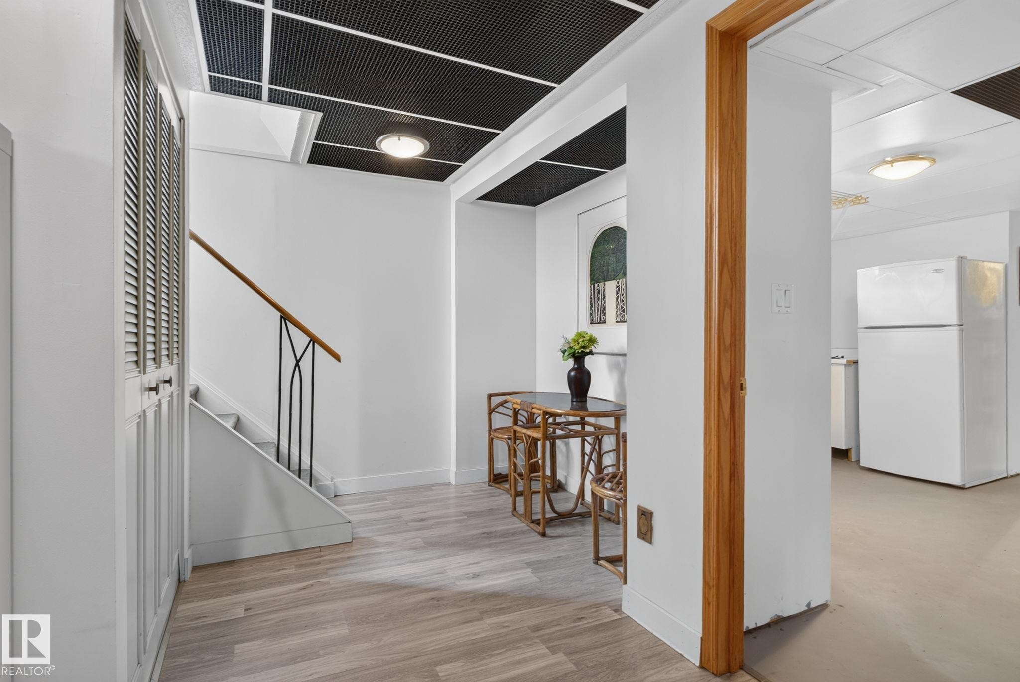 Interior space featuring light wood-finish flooring, white walls, and a black grid-patterned ceiling with flush-mount lighting - 7539 149A Avenue Nw, Edmonton, AB - Indoor Photo Showing Other Room