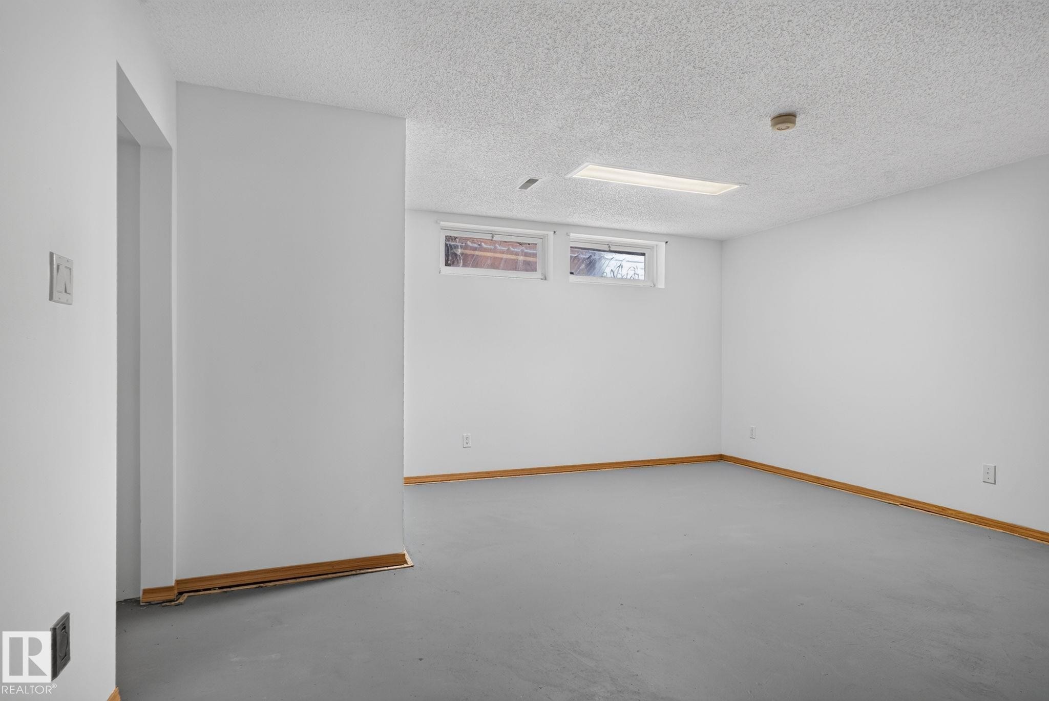 Spacious room featuring light gray flooring, white walls, and wood-finish baseboards - 7539 149A Avenue Nw, Edmonton, AB - Indoor