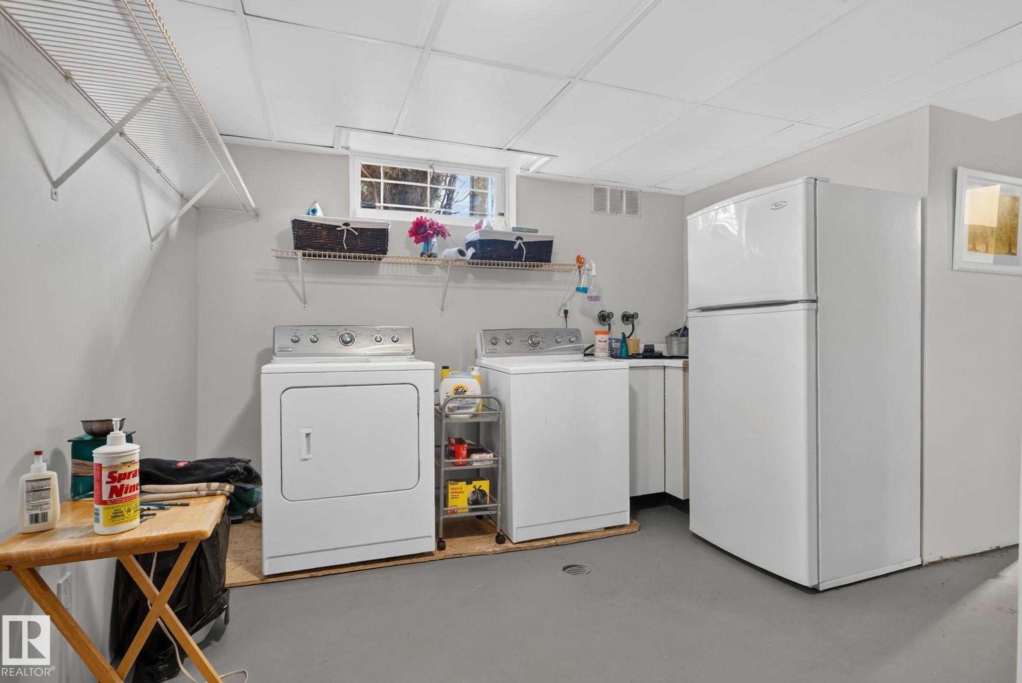 Dedicated laundry area featuring a washer and dryer, an additional refrigerator, white cabinetry, and overhead wire shelving - 7539 149A Avenue Nw, Edmonton, AB - Indoor Photo Showing Laundry Room
