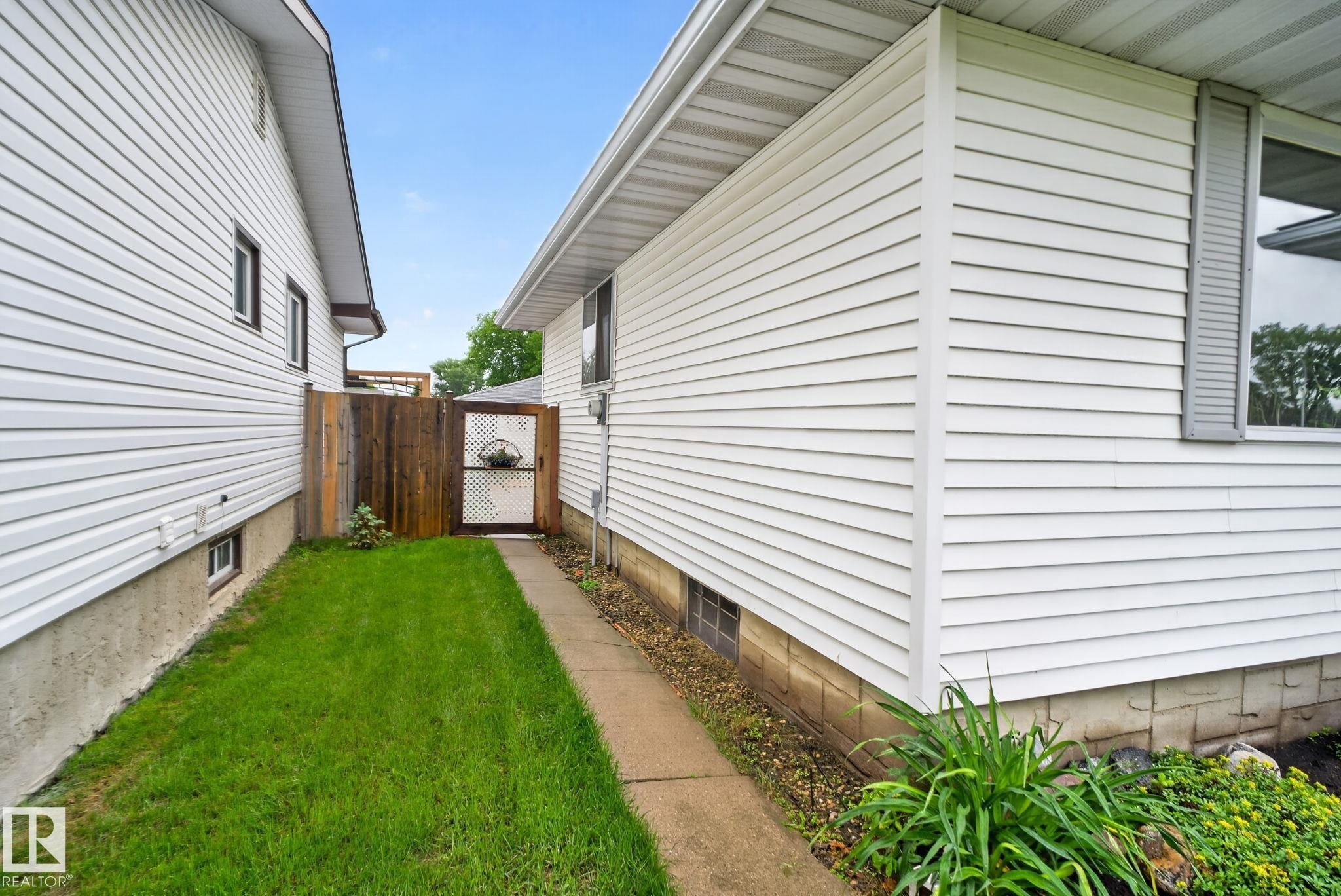 Side yard featuring a concrete pathway, a wooden fence with a lattice gate, and manicured lawn - 7539 149A Avenue Nw, Edmonton, AB - Outdoor With Exterior