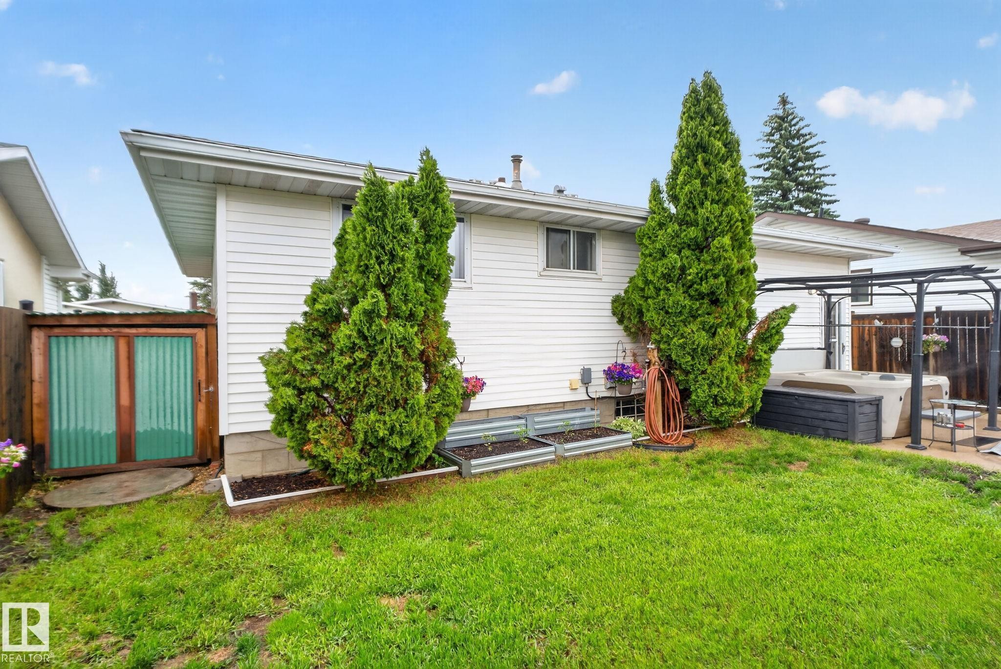 Expansive backyard featuring a manicured lawn, a built-in hot tub beneath a metal pergola, and two raised garden beds - 7539 149A Avenue Nw, Edmonton, AB - Outdoor With Exterior