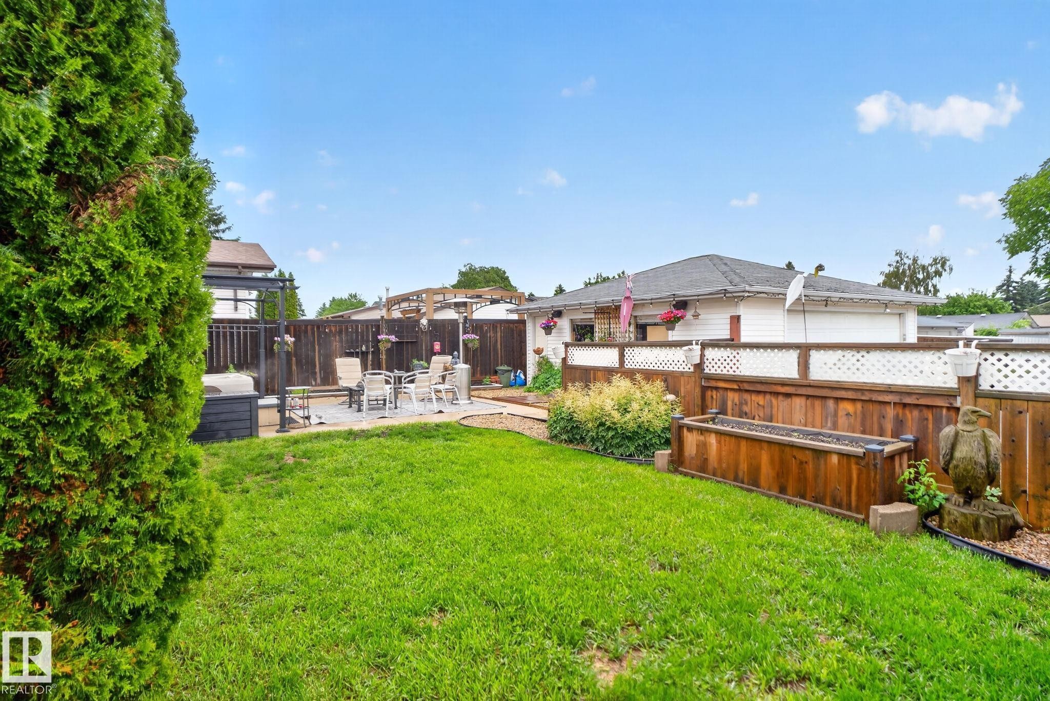 Manicured lawn with a paver patio area, bordered by a wood fence featuring white lattice accents - 7539 149A Avenue Nw, Edmonton, AB - Outdoor