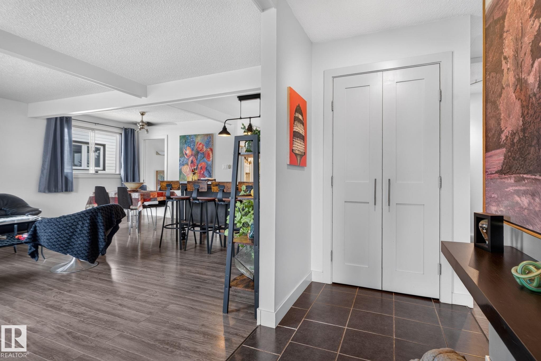 Entryway with dark tile flooring, leading to an open-concept living space featuring wood-finish flooring, white walls, and exposed ceiling beams - 7539 149A Avenue Nw, Edmonton, AB - Indoor Photo Showing Other Room