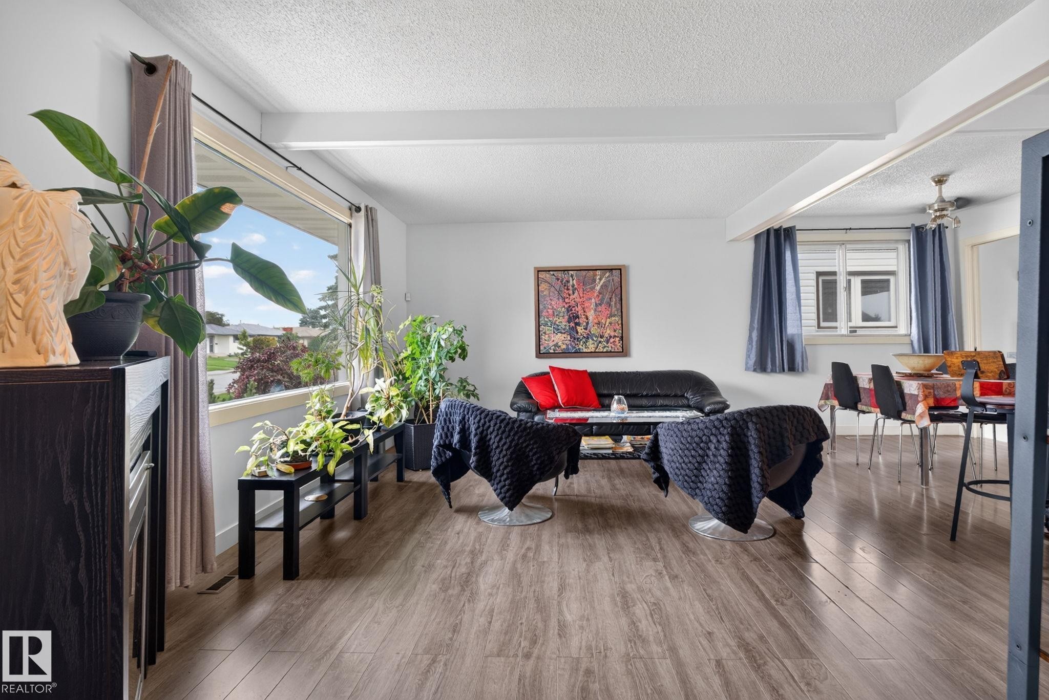 Spacious living area featuring wood-finish flooring, a large picture window, and exposed ceiling beams - 7539 149A Avenue Nw, Edmonton, AB - Indoor Photo Showing Other Room