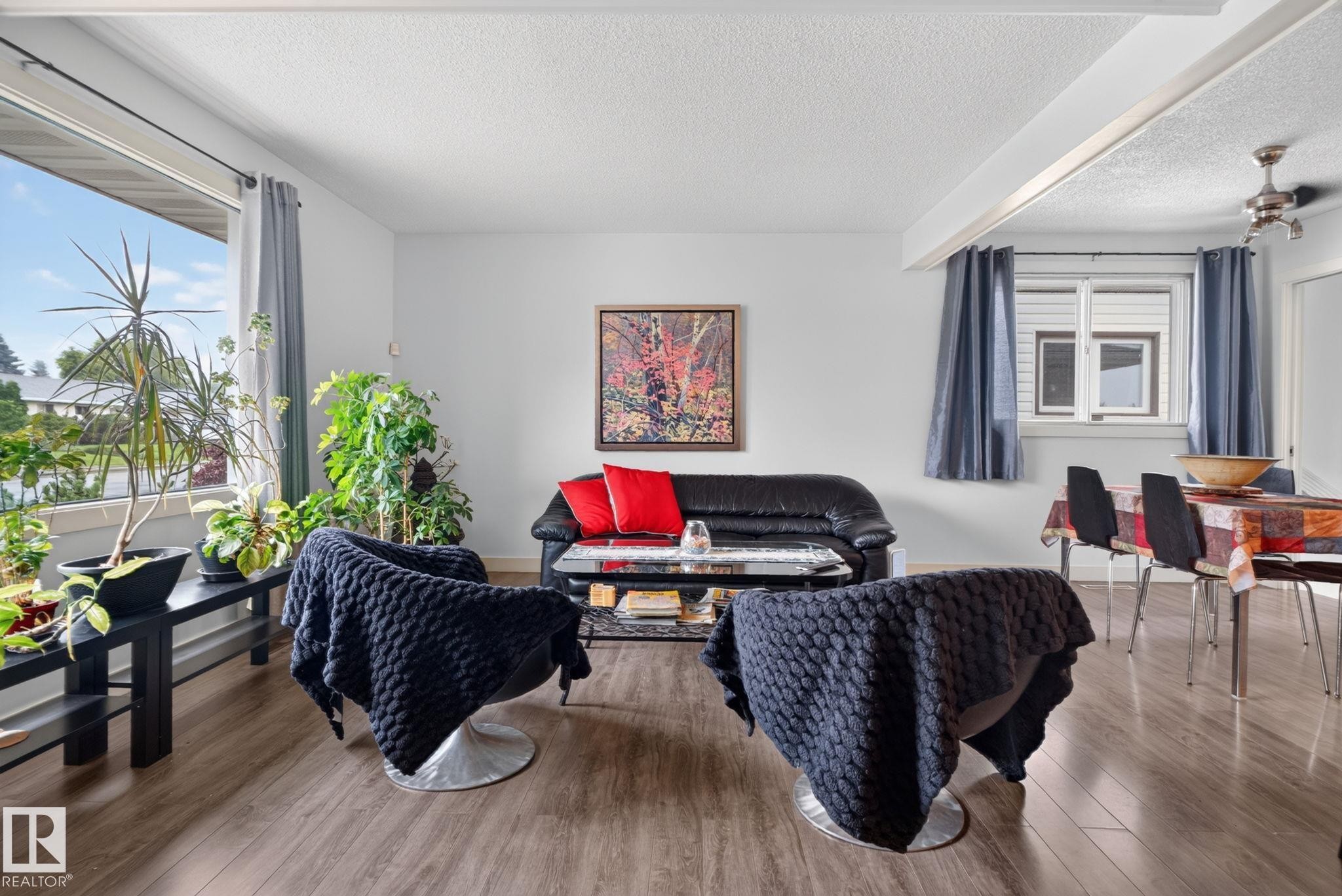 Open-concept living area with wood-finish flooring, a broad picture window, and a textured white ceiling - 7539 149A Avenue Nw, Edmonton, AB - Indoor Photo Showing Living Room
