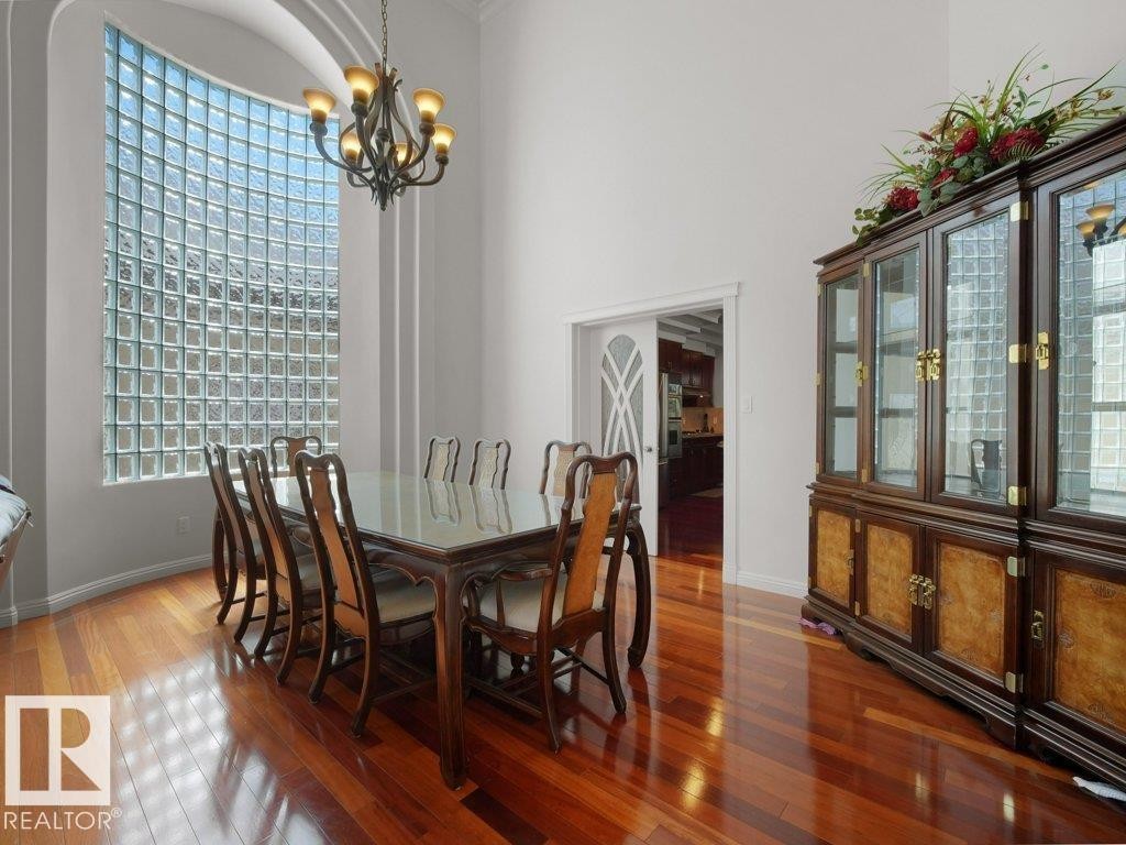 Formal dining area featuring a prominent glass block window, high ceilings, a chandelier, and rich wood-finish flooring - 2423 Tegler Green, Edmonton, AB