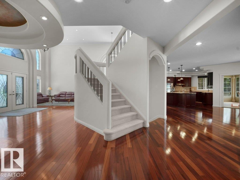 Grand entryway featuring a double staircase with metal balusters, hardwood flooring, and a two-story foyer with decorative arched windows - 2423 Tegler Green, Edmonton, AB