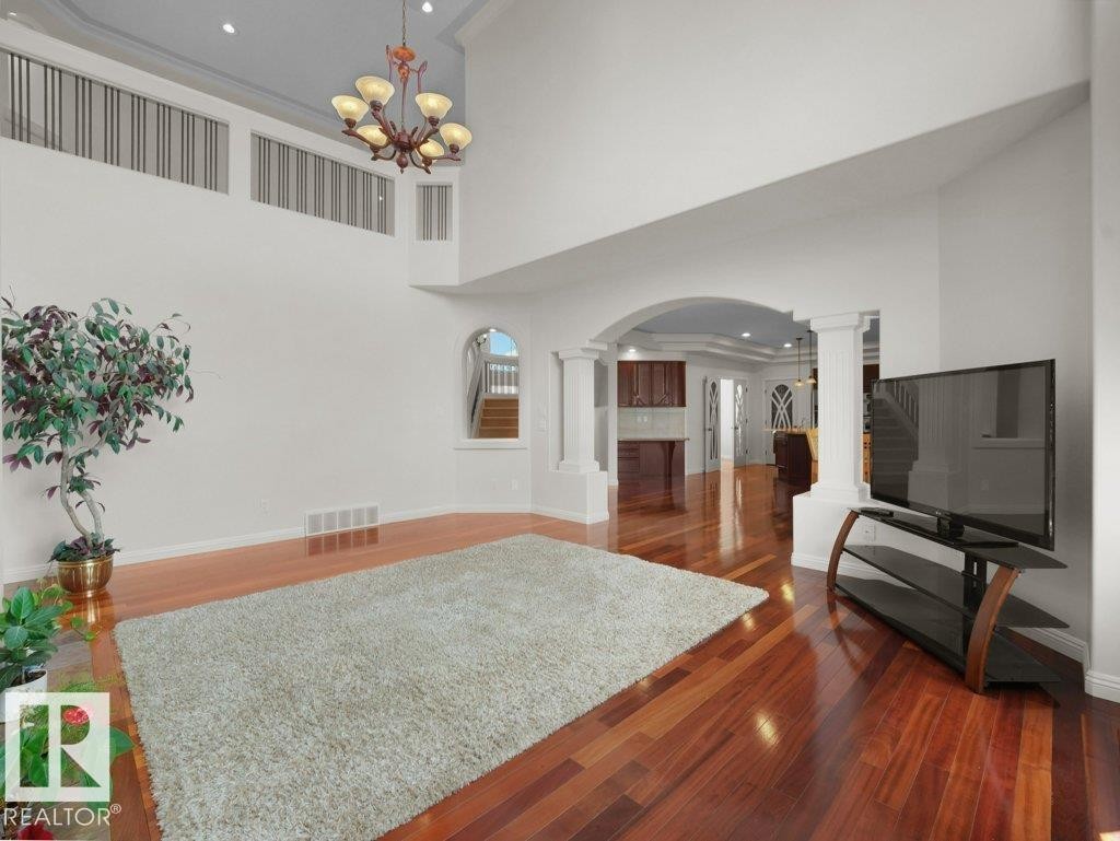 Spacious living area featuring high ceilings, rich wood-finish flooring, and an elegant chandelier - 2423 Tegler Green, Edmonton, AB