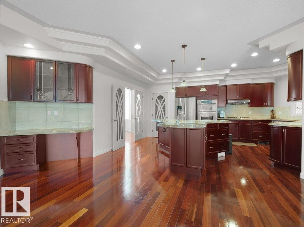 Spacious kitchen featuring rich wood-finish cabinetry, a central island with integrated seating, recessed lighting, and pendant fixtures - 2423 Tegler Green, Edmonton, AB
