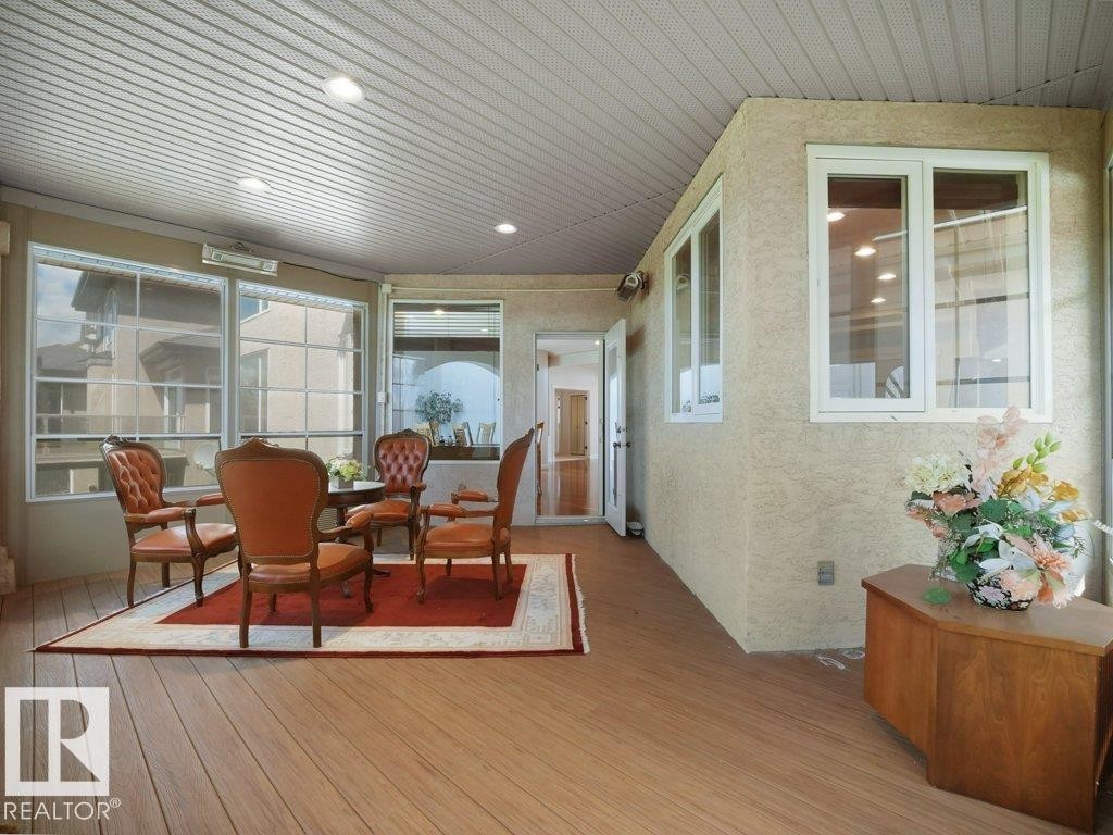 Enclosed patio with wood-finish flooring, white vinyl windows, recessed lighting, and a textured stucco exterior wall - 2423 Tegler Green, Edmonton, AB