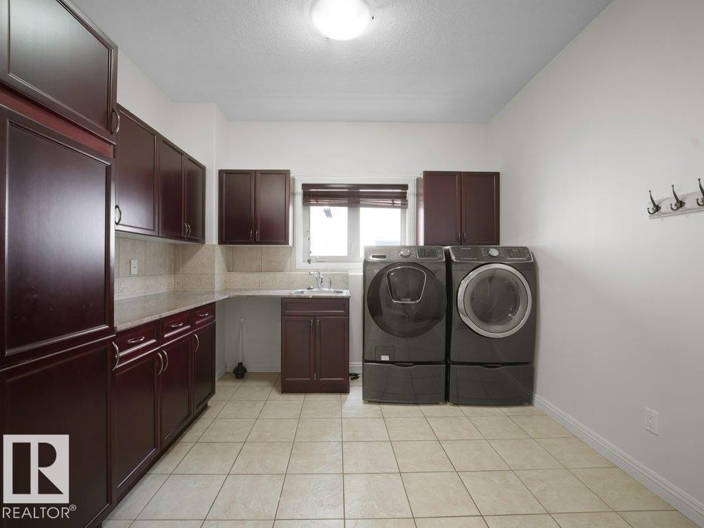Laundry area featuring extensive dark wood cabinetry, light tile flooring, solid surface countertops, and a utility sink - 2423 Tegler Green, Edmonton, AB