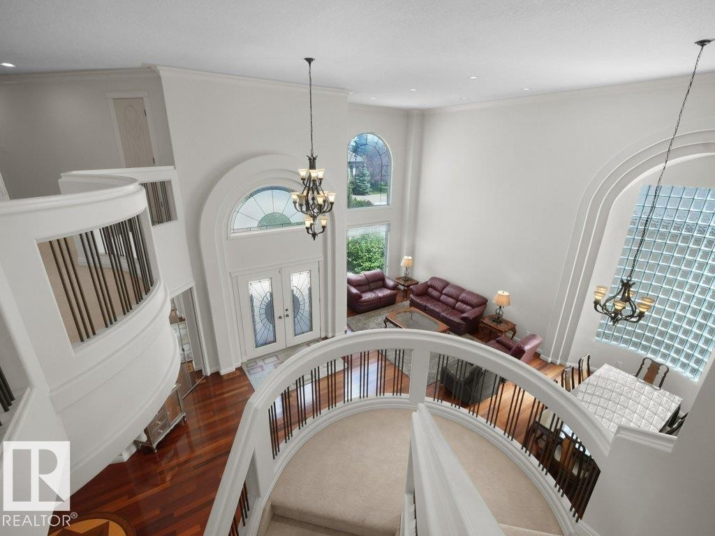 Two-story foyer with a grand curved staircase, wrought iron balusters, and wood-finish flooring - 2423 Tegler Green, Edmonton, AB