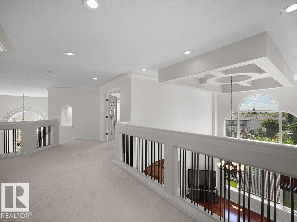 Open loft area featuring recessed lighting, a decorative ceiling fixture, arched windows, light-toned carpeting, and white balusters with dark vertical spindles - 2423 Tegler Green, Edmonton, AB