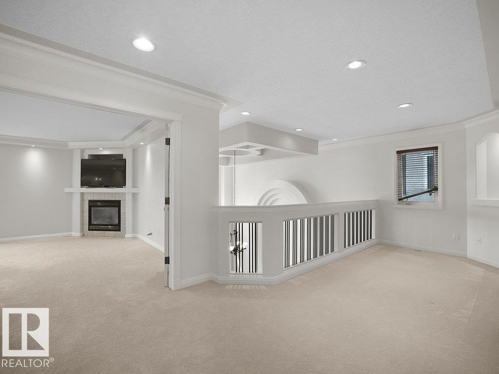 Carpeted room featuring a built-in fireplace with a tiled surround, recessed lighting, crown molding, and a partial balustrade - 2423 Tegler Green, Edmonton, AB