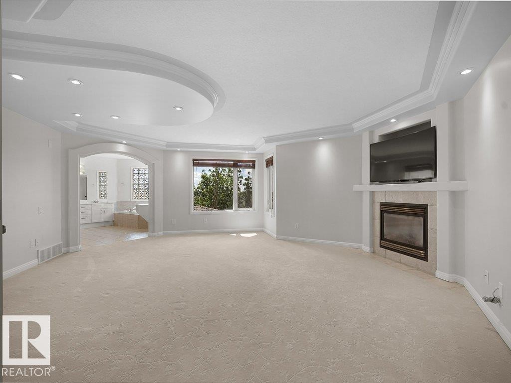 Spacious room featuring a tray ceiling with recessed lighting, a fireplace with a stone surround, and an arched doorway leading to an additional space - 2423 Tegler Green, Edmonton, AB