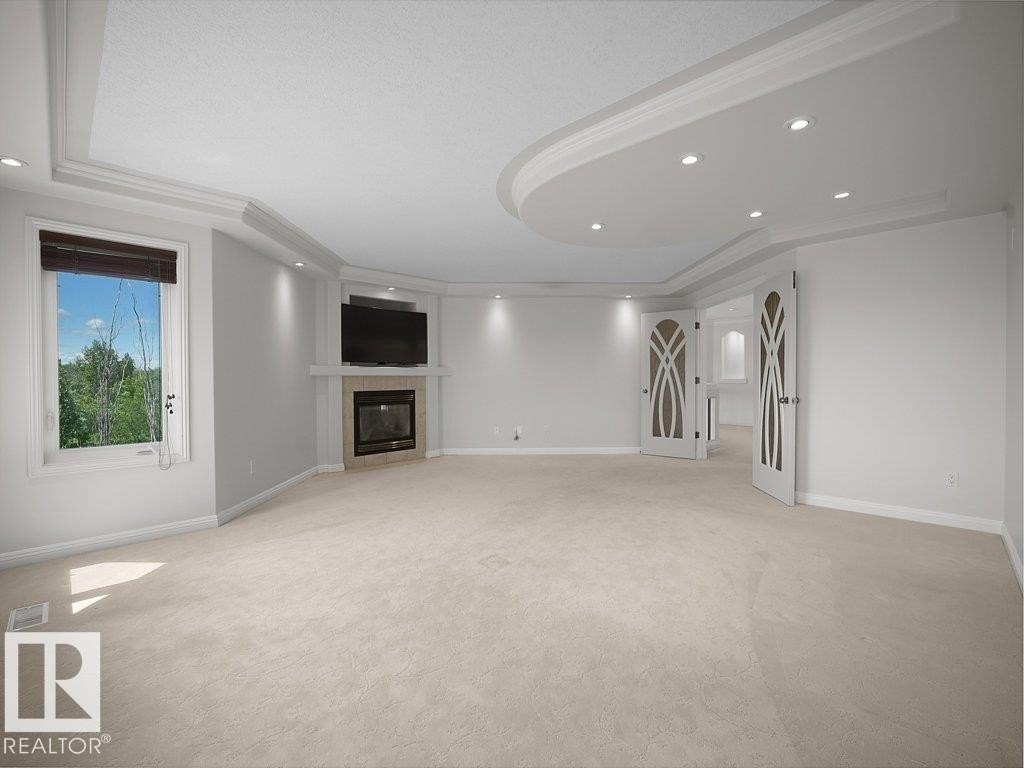 Spacious room featuring a corner fireplace with a stone surround, a large window, and light-colored carpeting - 2423 Tegler Green, Edmonton, AB