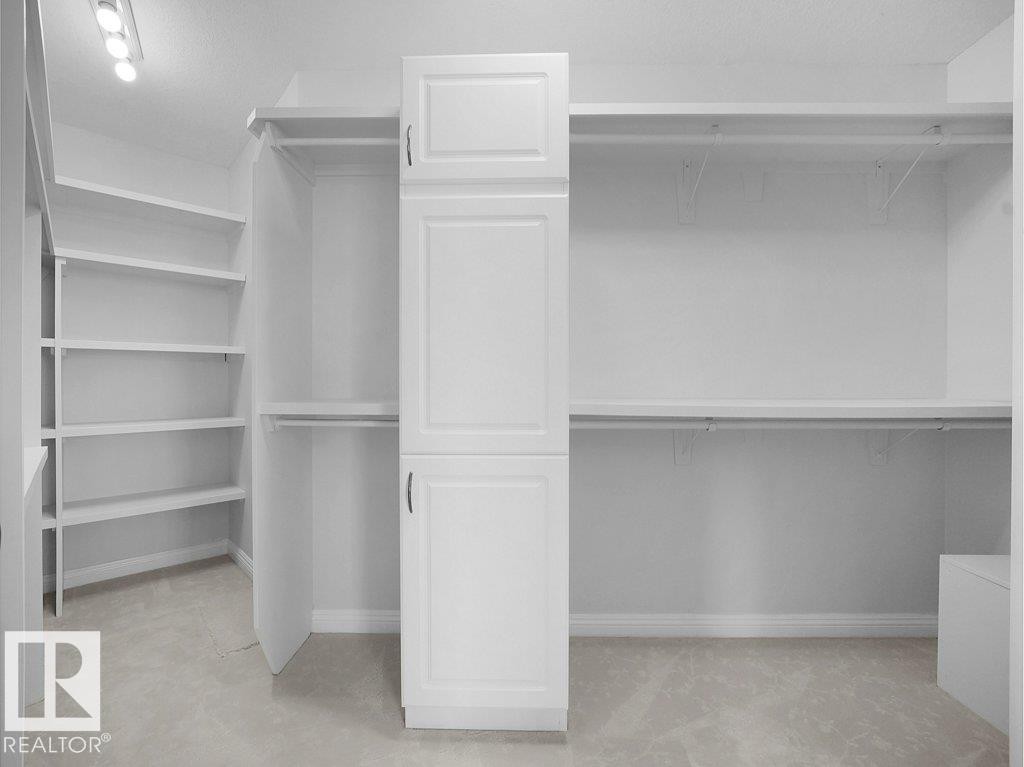 Spacious walk-in closet featuring built-in white cabinetry, extensive shelving, hanging rods, and recessed ceiling lighting - 2423 Tegler Green, Edmonton, AB