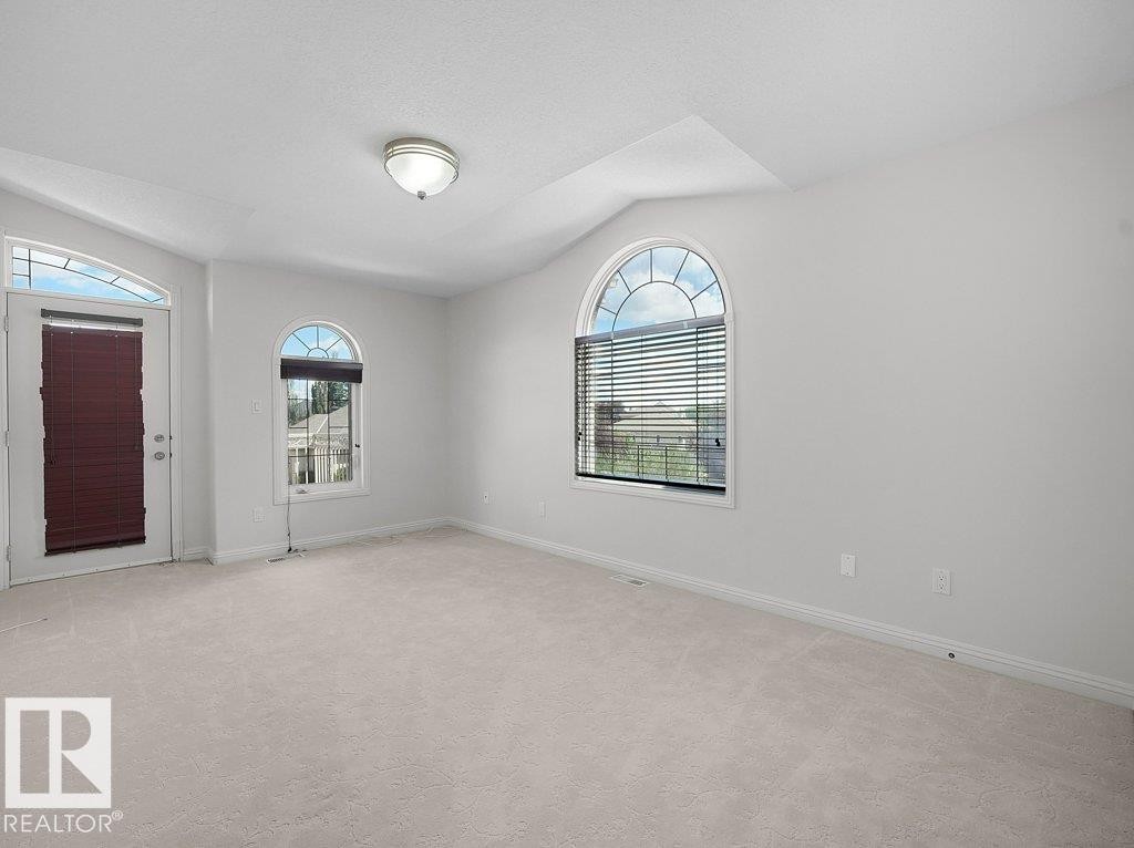 Carpeted room featuring multiple arched windows with blinds, a white door with an arched transom, and a flush-mount ceiling light fixture - 2423 Tegler Green, Edmonton, AB