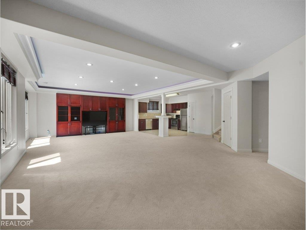Spacious entertainment area featuring built-in cabinetry, recessed lighting, neutral carpeting, and a visible kitchen area - 2423 Tegler Green, Edmonton, AB