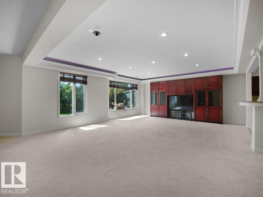 Spacious interior room featuring light-toned carpeting, multiple windows with natural light, and a built-in entertainment unit with rich wood-finish cabinetry - 2423 Tegler Green, Edmonton, AB