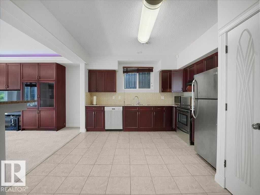 Kitchen featuring wood-finish cabinetry, stainless steel appliances, and tile flooring - 2423 Tegler Green, Edmonton, AB