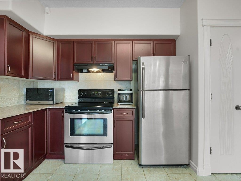 Cherry-toned cabinetry with stainless steel appliances, including a refrigerator and range oven - 2423 Tegler Green, Edmonton, AB