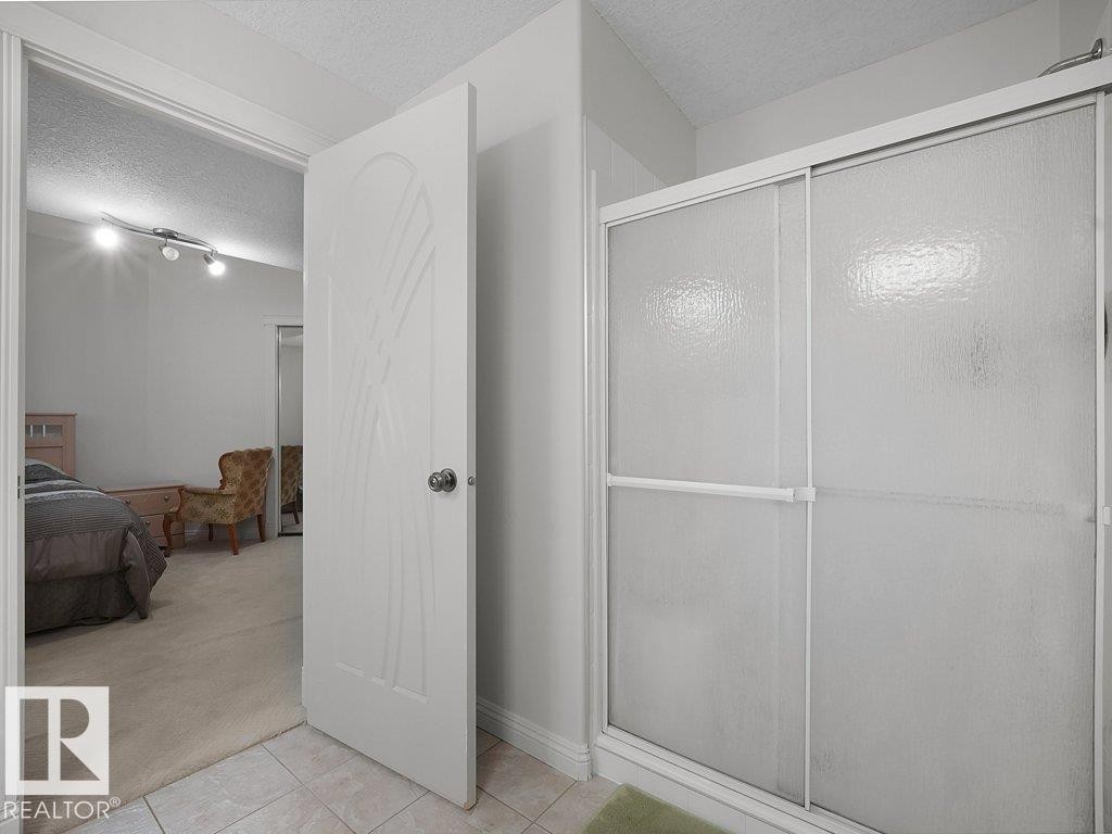 Shower enclosure with textured glass sliding doors, framed by light-toned wall paint and ceramic tile flooring - 2423 Tegler Green, Edmonton, AB