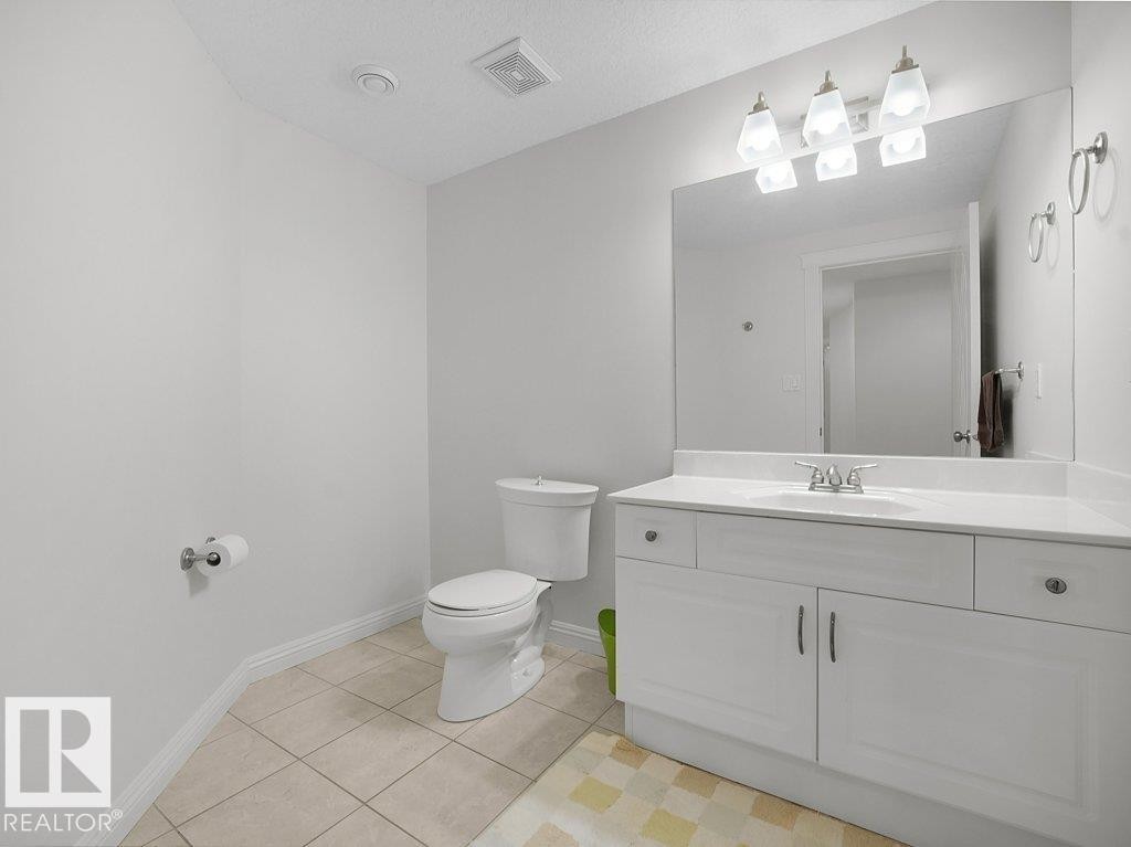 Bathroom featuring a white vanity with integrated sink, a large wall-mounted mirror, brushed nickel light fixture, and tile flooring - 2423 Tegler Green, Edmonton, AB