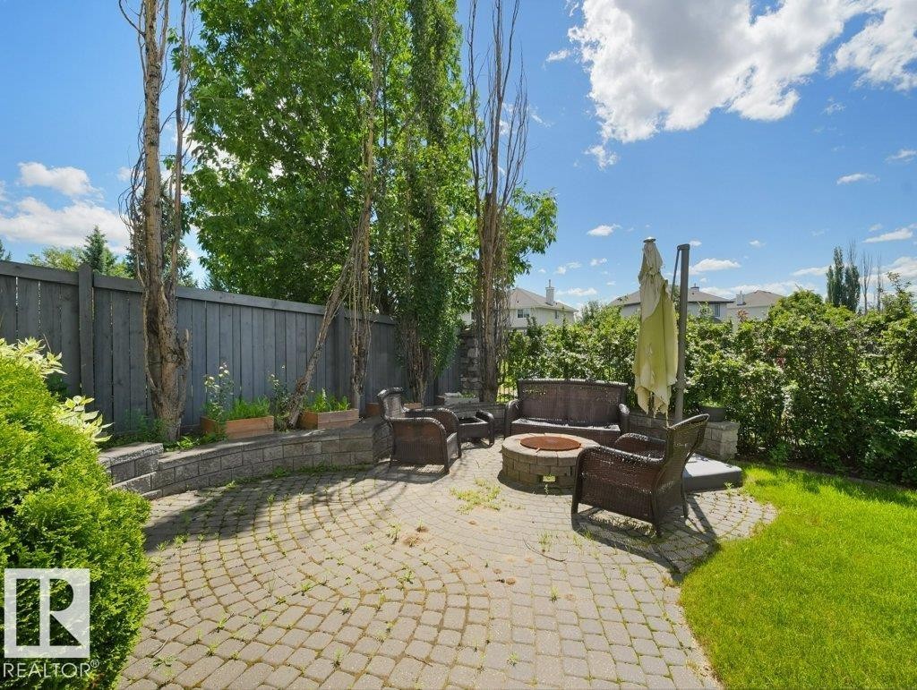 Outdoor patio with paver stone surface, built-in stone fire pit, wood privacy fence, and mature perimeter landscaping - 2423 Tegler Green, Edmonton, AB