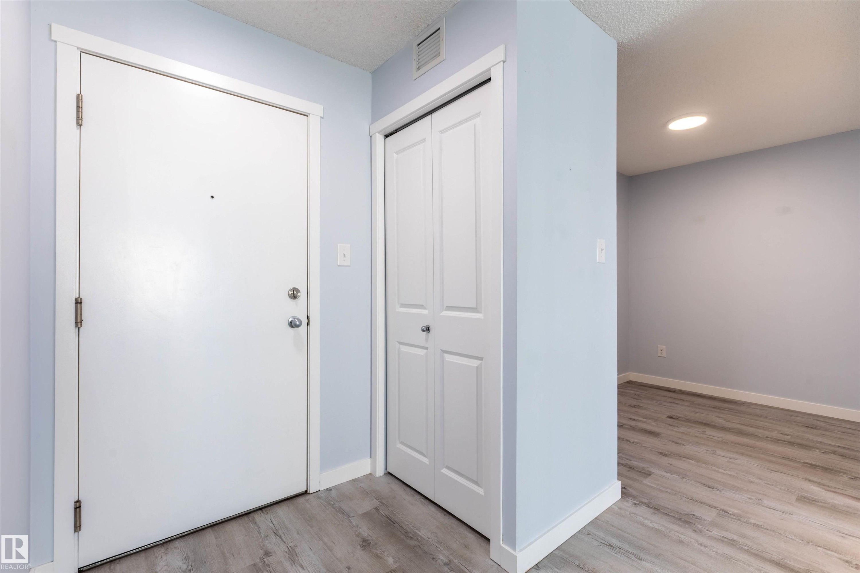 Entryway featuring a solid core door, bifold closet doors, light blue wall paint, white trim, and wood-finish flooring - 403 25 Element Dr, St. Albert, AB - Indoor Photo Showing Other Room