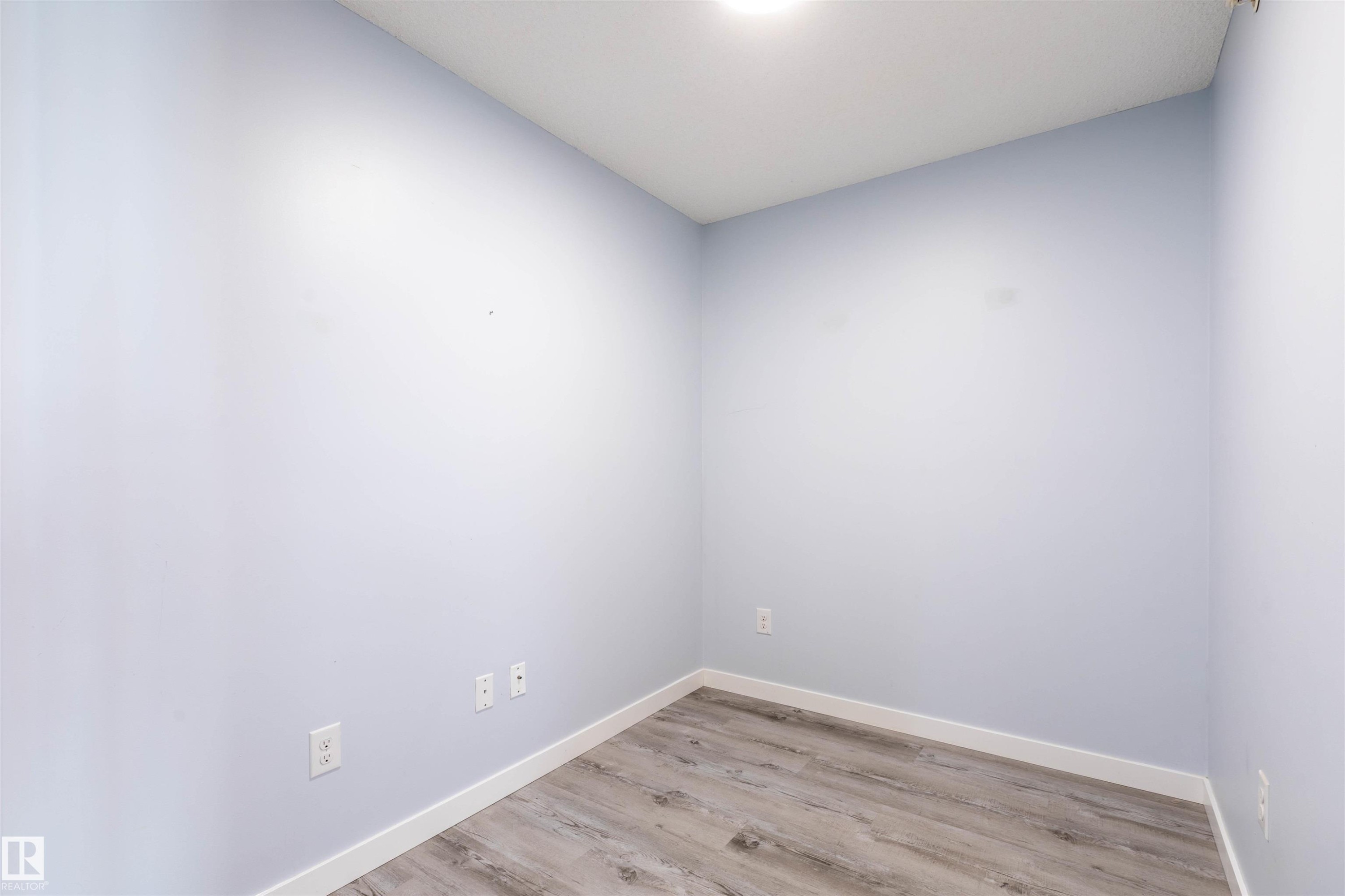 Interior room featuring light blue walls, wood-finish flooring, white baseboards, and a ceiling-mounted light fixture - 403 25 Element Dr, St. Albert, AB - Indoor Photo Showing Other Room