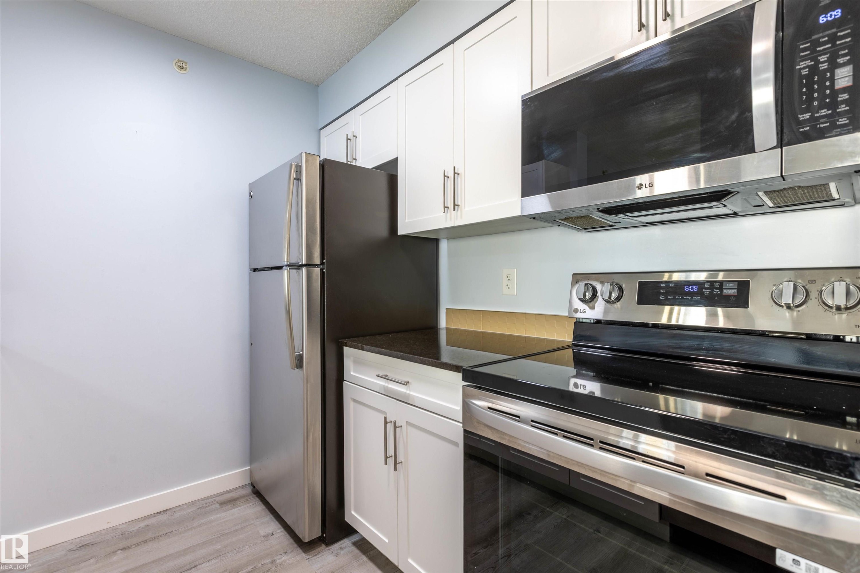 Modern kitchen featuring white shaker cabinetry, dark countertops, and stainless steel appliances including a refrigerator, range, and microwave - 403 25 Element Dr, St. Albert, AB - Indoor Photo Showing Kitchen