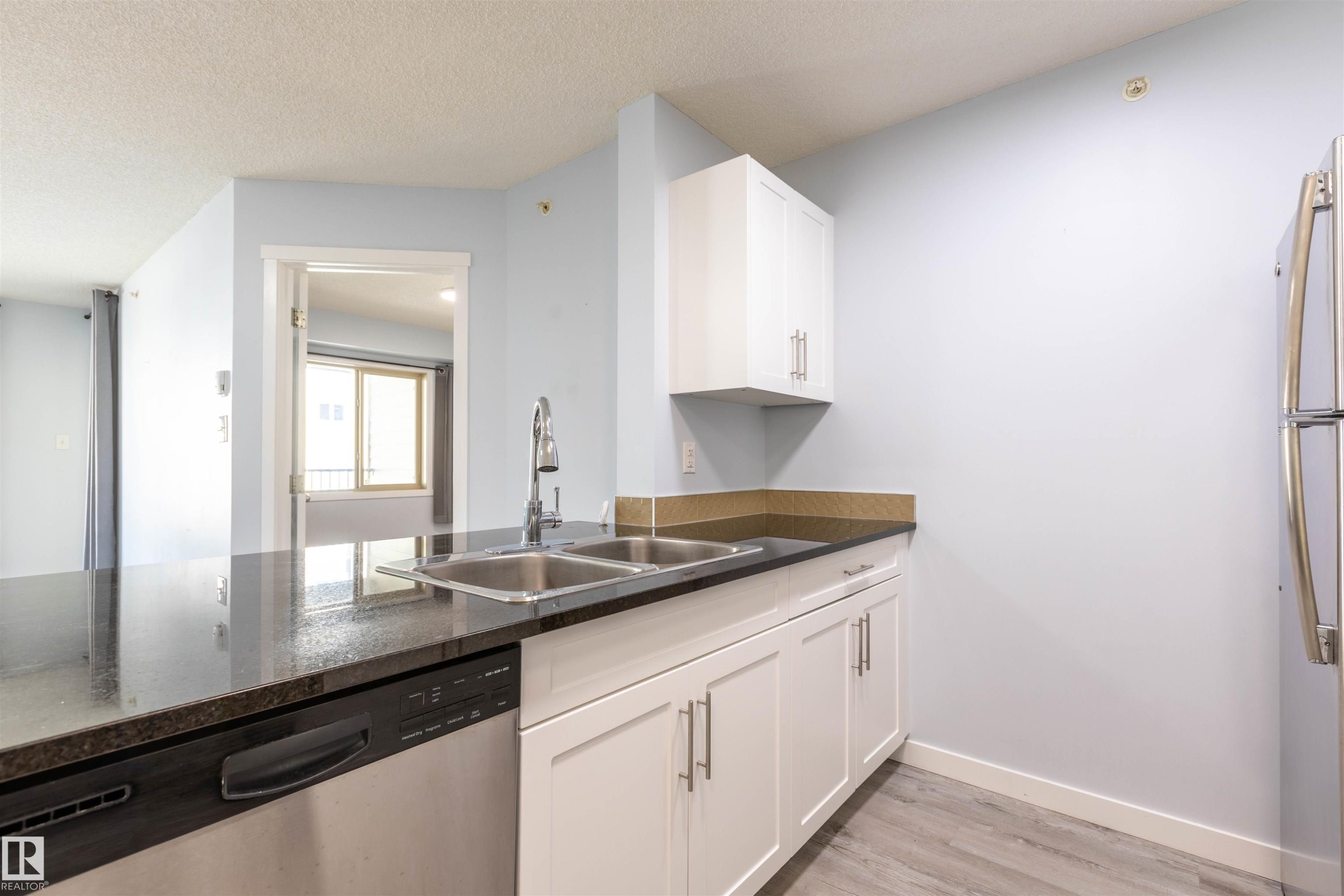 Kitchen featuring stainless steel double basin sink, chrome faucet, black granite-look countertops, white cabinetry with brushed nickel pulls, and a stainless steel dishwasher - 403 25 Element Dr, St. Albert, AB - Indoor Photo Showing Kitchen With Double Sink
