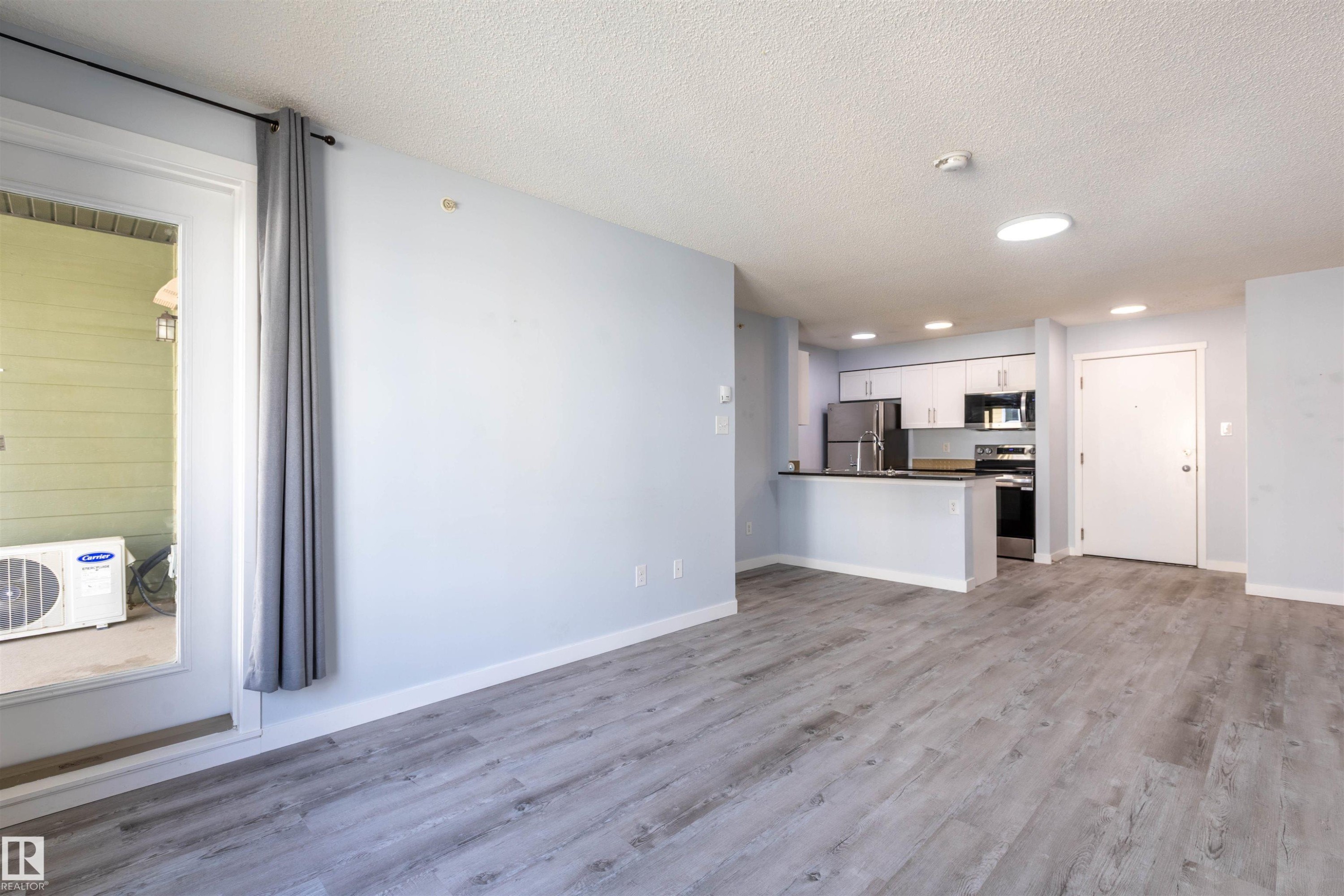 Open-concept living space featuring wood-finish flooring, light blue walls, a kitchen with white cabinetry, stainless steel appliances, and recessed lighting - 403 25 Element Dr, St. Albert, AB - Indoor Photo Showing Kitchen