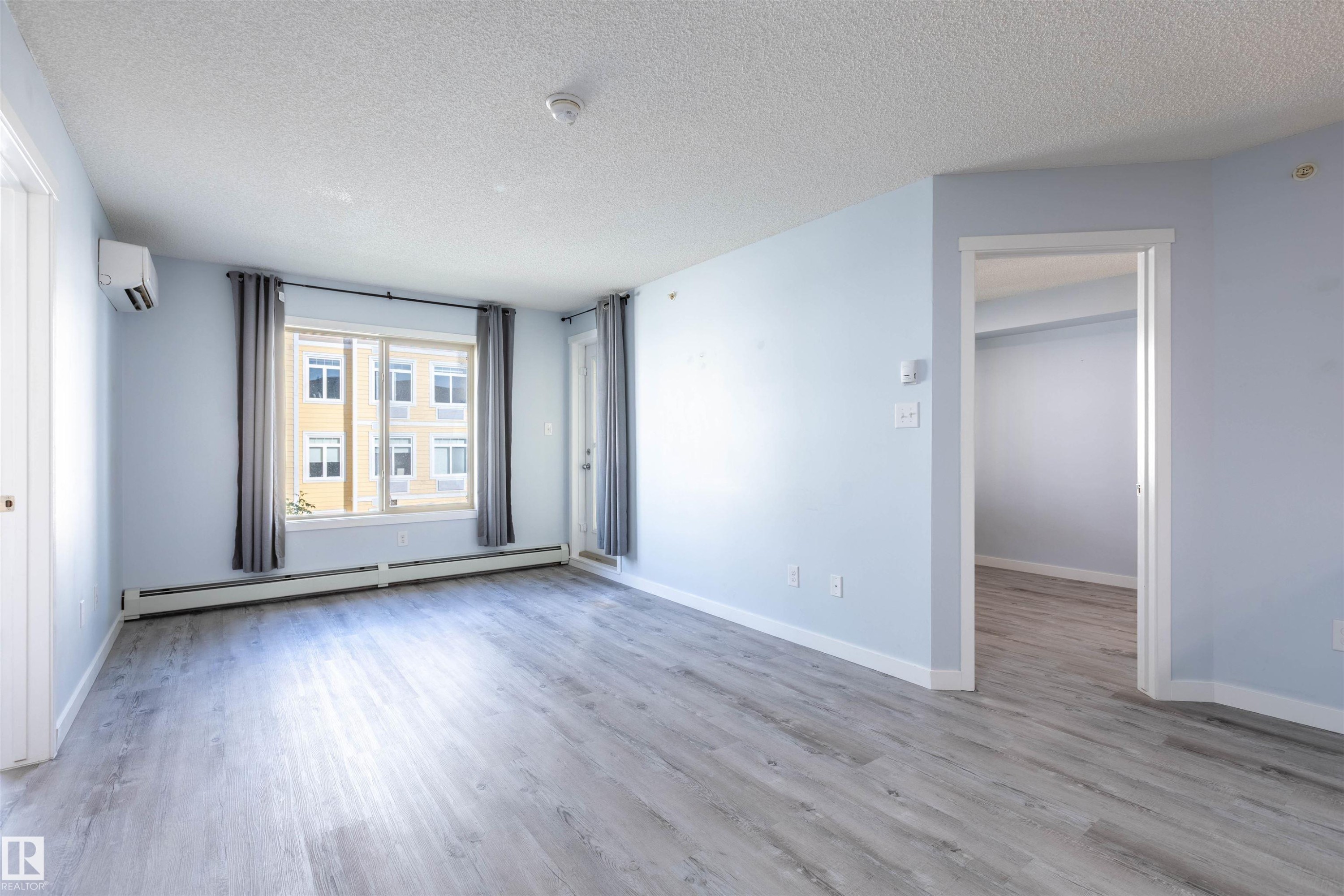 Spacious room featuring wood-finish flooring, light blue walls, and a large window with privacy drapes - 403 25 Element Dr, St. Albert, AB - Indoor Photo Showing Other Room