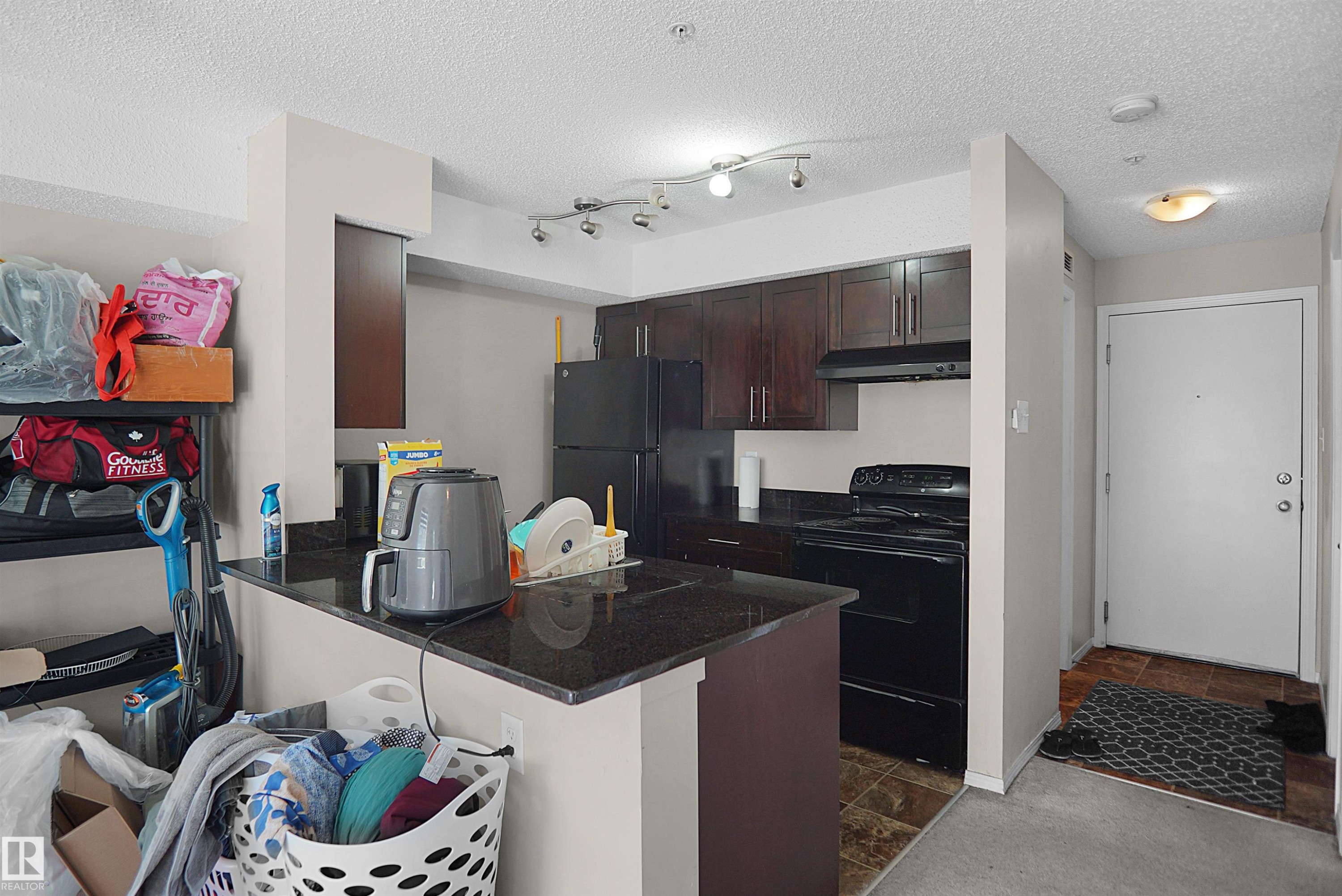 Kitchen featuring wood-finish cabinetry, black appliances, and dark granite countertops - 215 1070 Mcconachie Blvd, Edmonton, AB