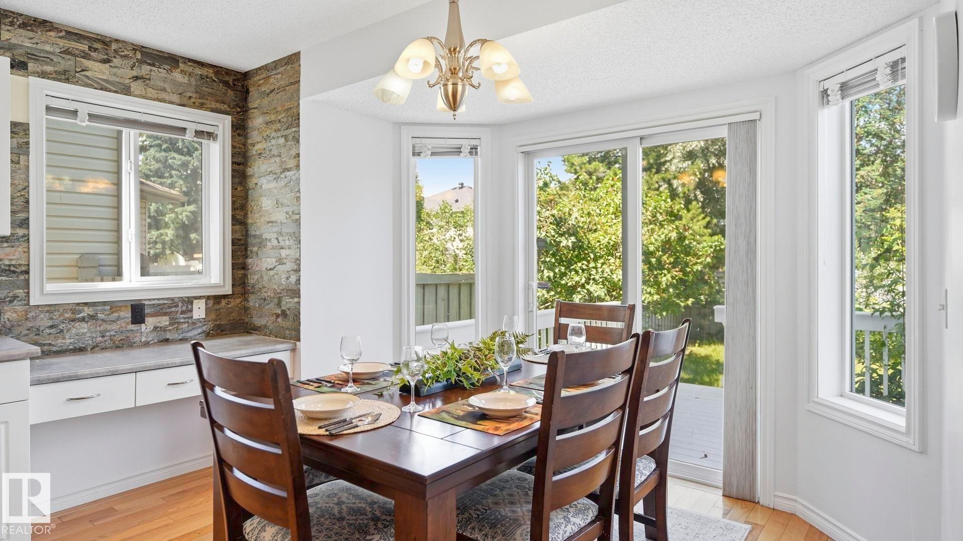 Dining area featuring a wood-finish table, a decorative light fixture, and abundant natural light from multiple windows - 3591 Mclean Crescent, Edmonton, AB