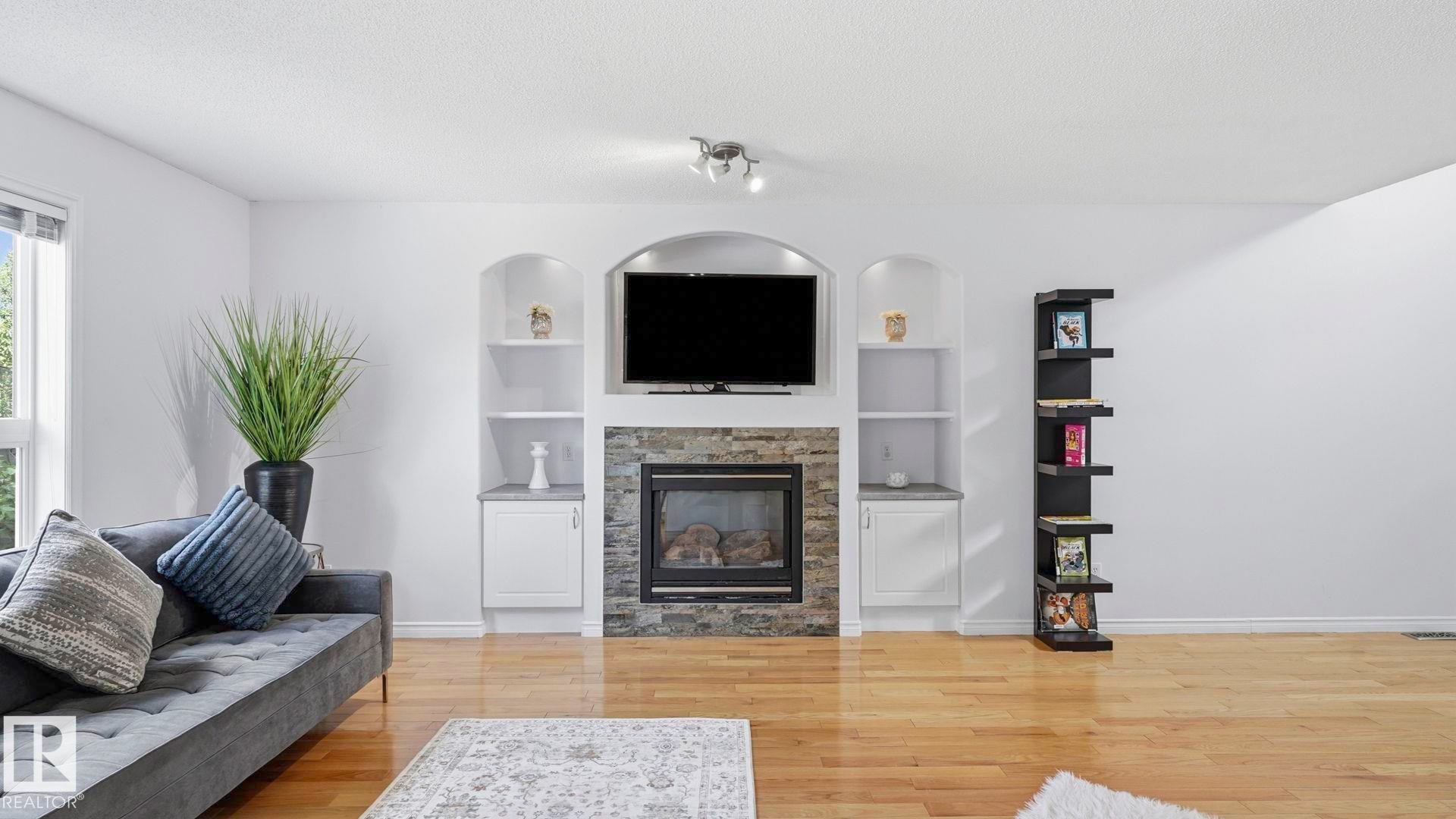 Living area featuring a stone-clad fireplace with a built-in media center, recessed shelving, and integrated cabinetry - 3591 Mclean Crescent, Edmonton, AB