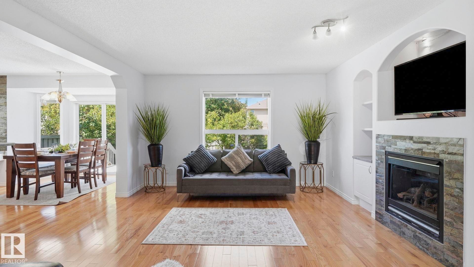 Bright living space featuring wood-finish flooring, a contemporary fireplace with a stacked stone surround, and an arched built-in media niche - 3591 Mclean Crescent, Edmonton, AB