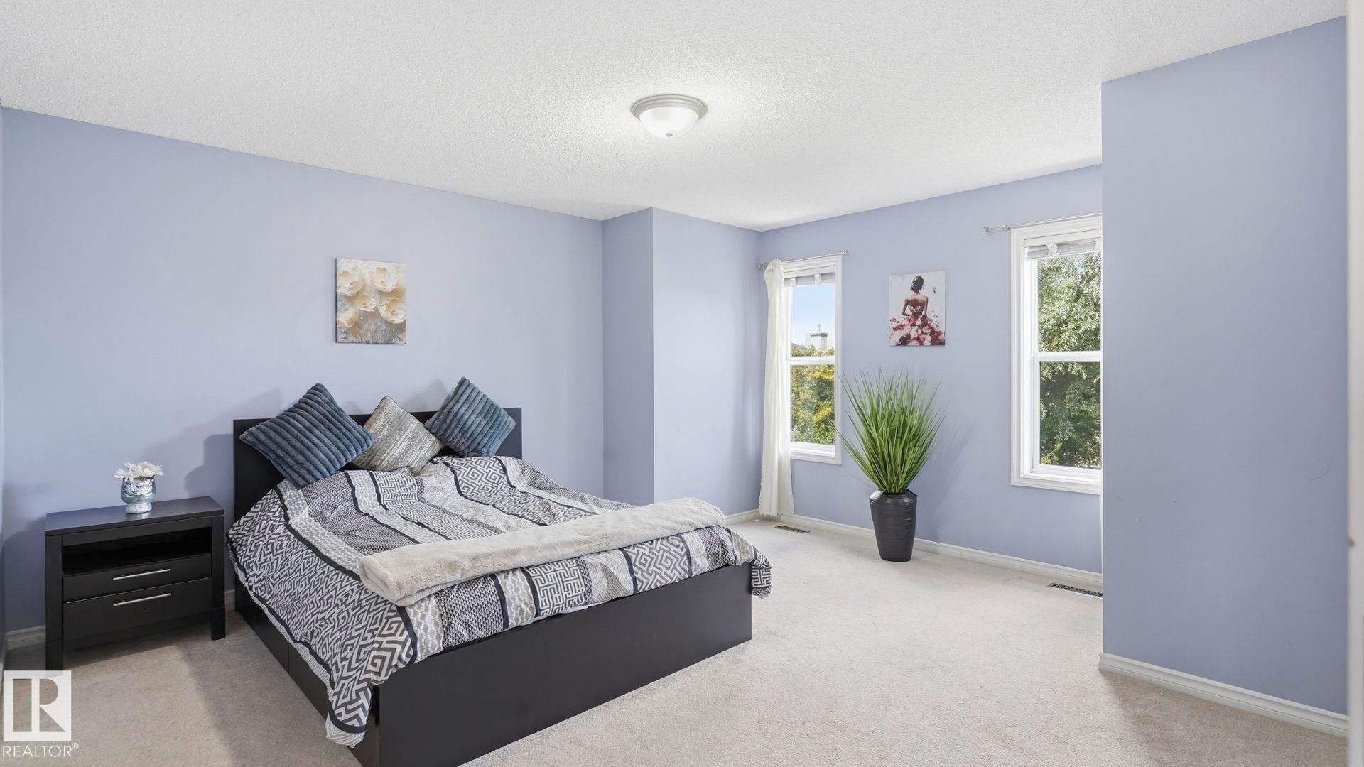 Spacious room featuring light lavender walls, plush carpeting, two large windows, a textured ceiling, and a flush mount ceiling light fixture - 3591 Mclean Crescent, Edmonton, AB