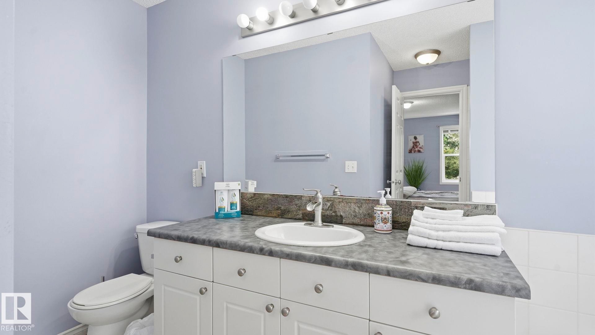 Bathroom featuring a white vanity with a dark countertop, an undermount sink, and a large wall-mounted mirror - 3591 Mclean Crescent, Edmonton, AB