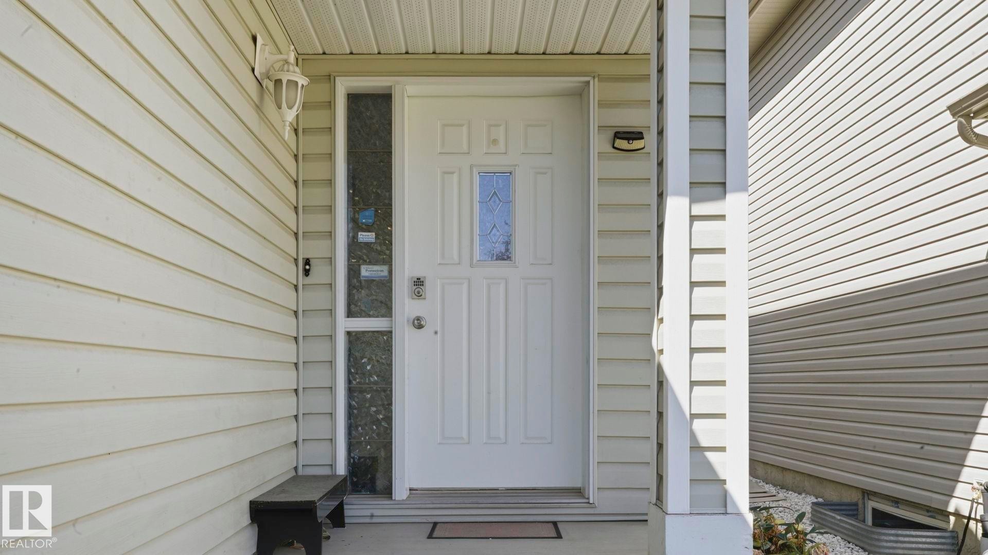 Front entry featuring a white paneled door with decorative glass insert, sidelight, and an overhead porch light - 3591 Mclean Crescent, Edmonton, AB