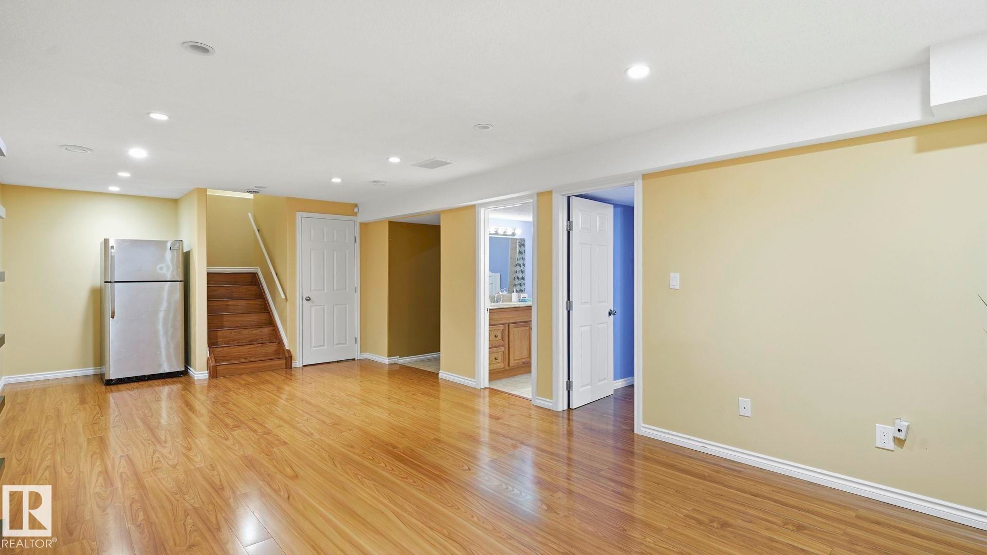Spacious room featuring wood-finish flooring, recessed lighting, and a stainless steel refrigerator - 3591 Mclean Crescent, Edmonton, AB
