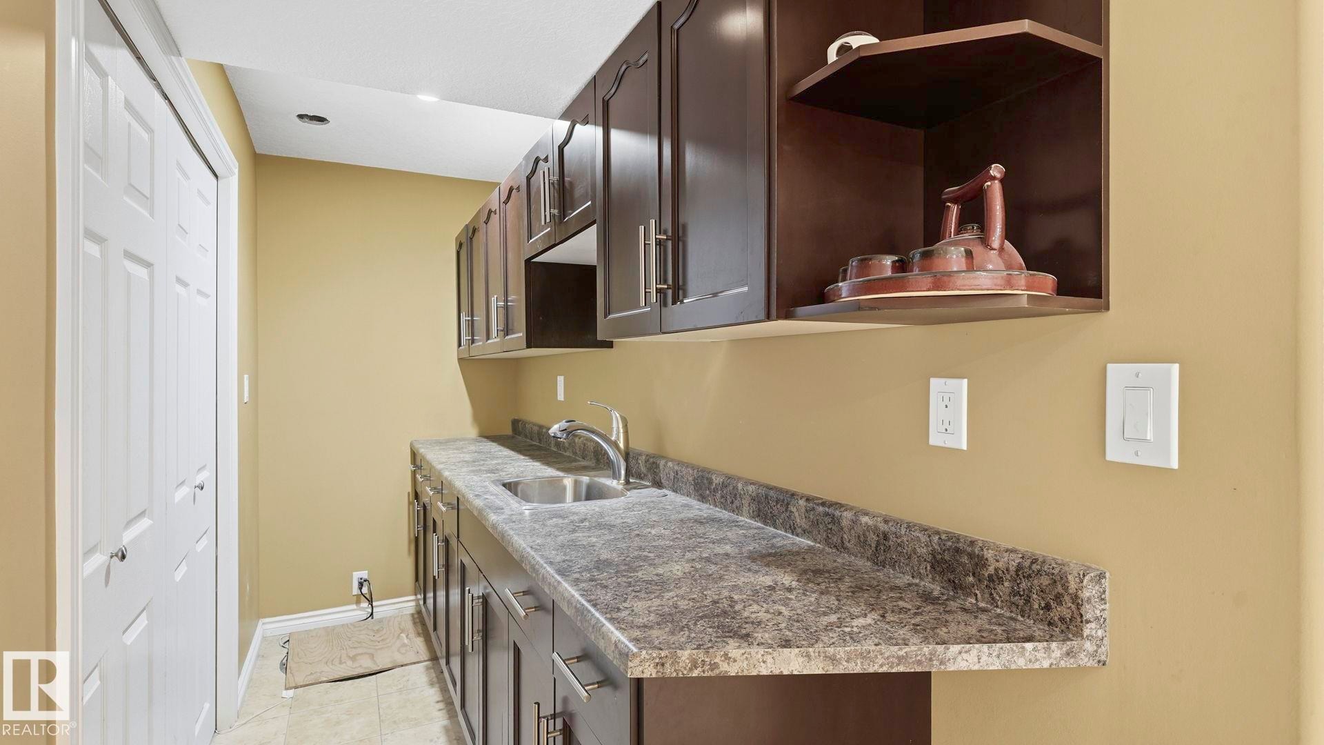 Utility area featuring dark wood-finish cabinetry, a stainless steel sink, and a speckled countertop - 3591 Mclean Crescent, Edmonton, AB