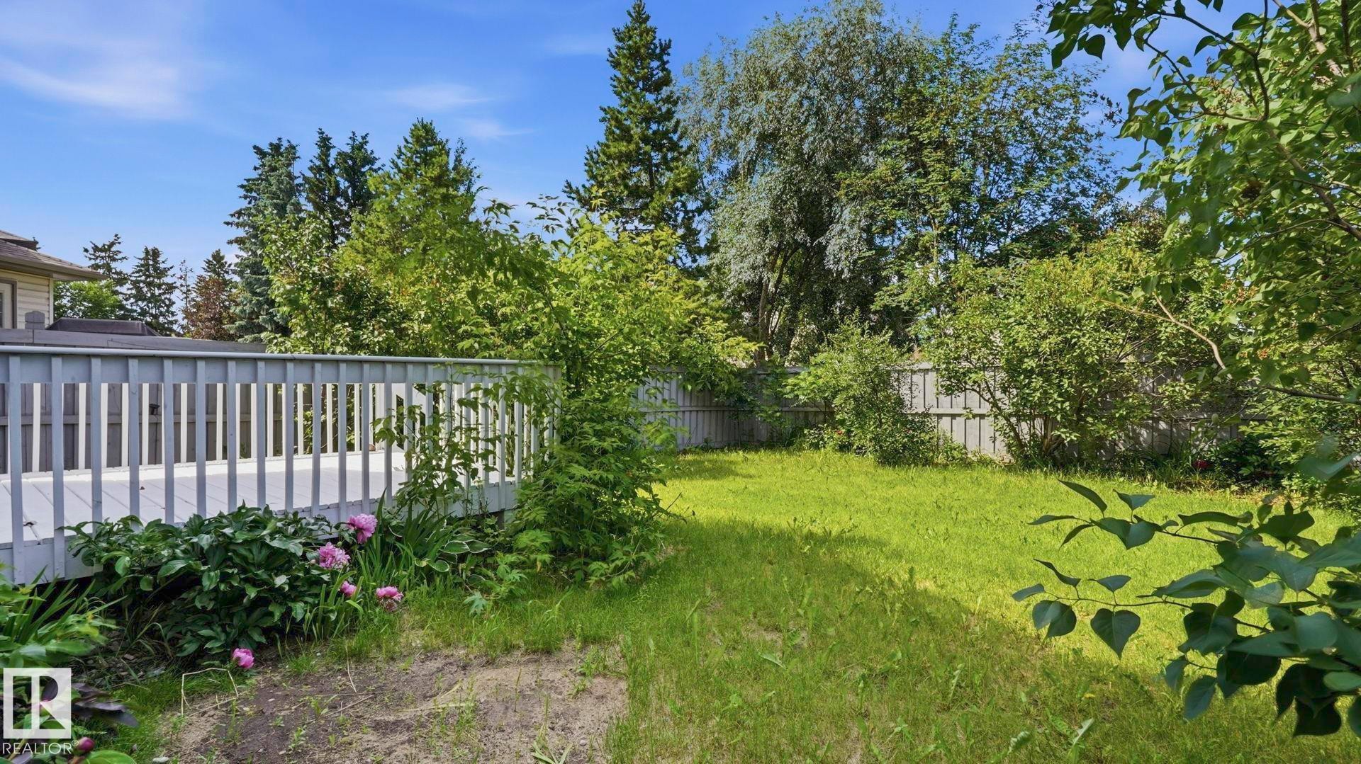 Spacious backyard featuring a wooden deck with railing, a grass lawn, mature trees, and perimeter fencing - 3591 Mclean Crescent, Edmonton, AB