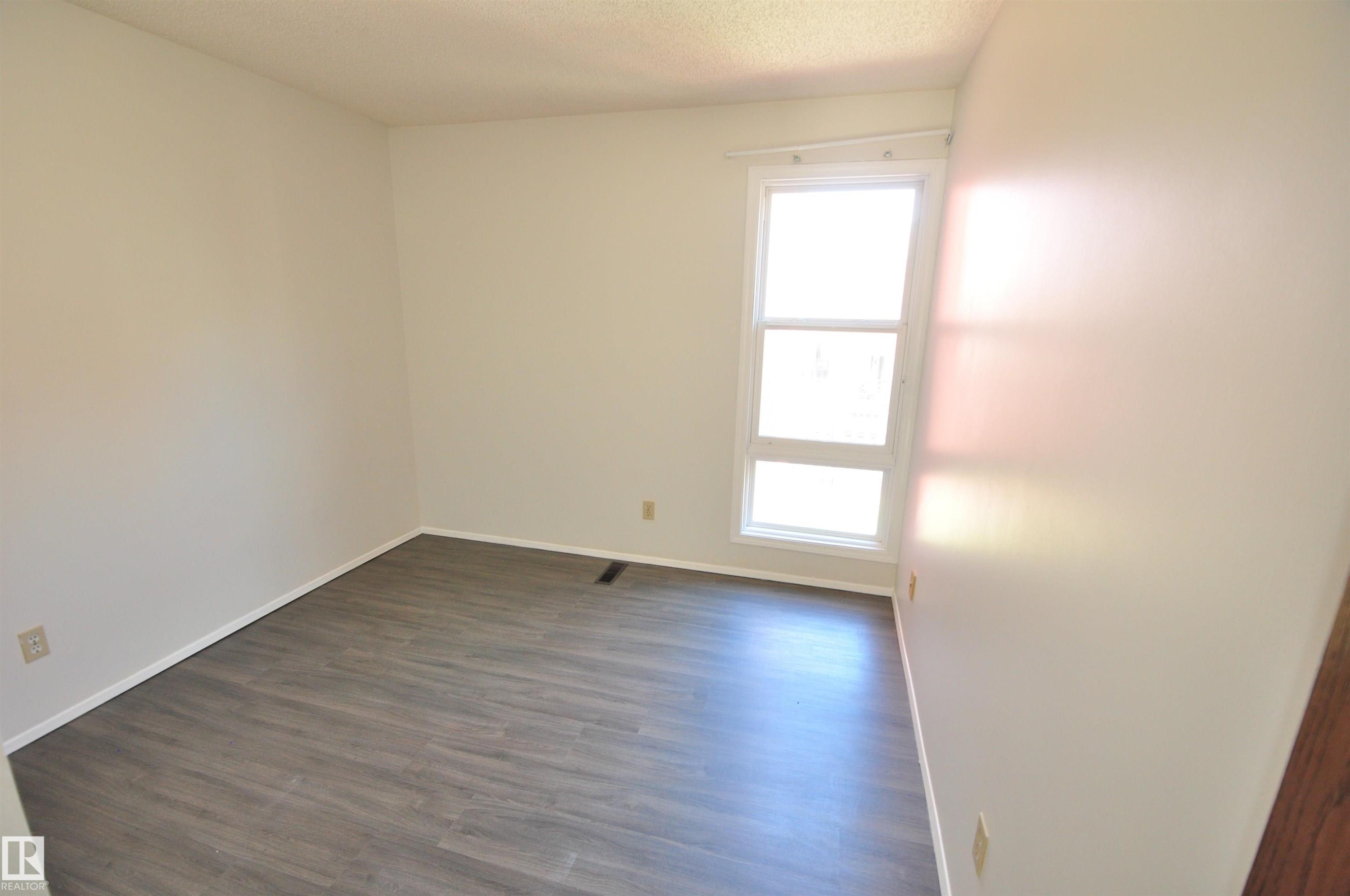 Room featuring wood-finish flooring, light-toned walls, white baseboards, and a bright window with white trim - 617 Millbourne Road E, Edmonton, AB