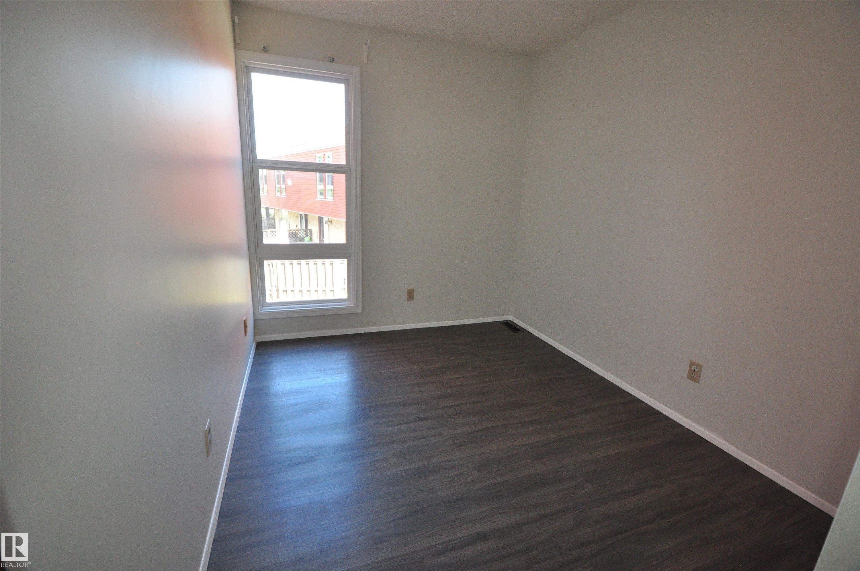 Contemporary room featuring dark wood-finish flooring, light neutral wall paint, and a large multi-pane window with white trim - 617 Millbourne Road E, Edmonton, AB